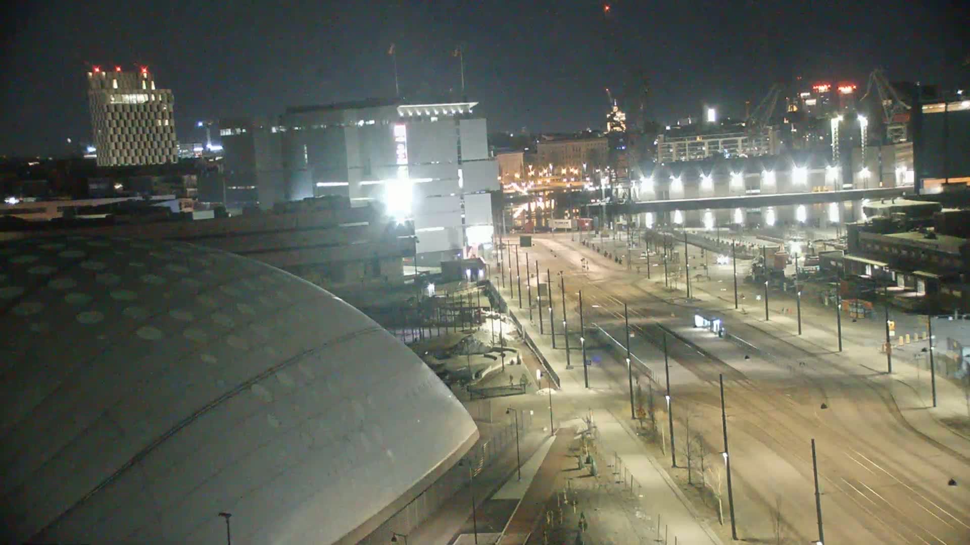 A nighttime view of a city featuring a large, domed building, several other structures, and empty streets with streetlights.