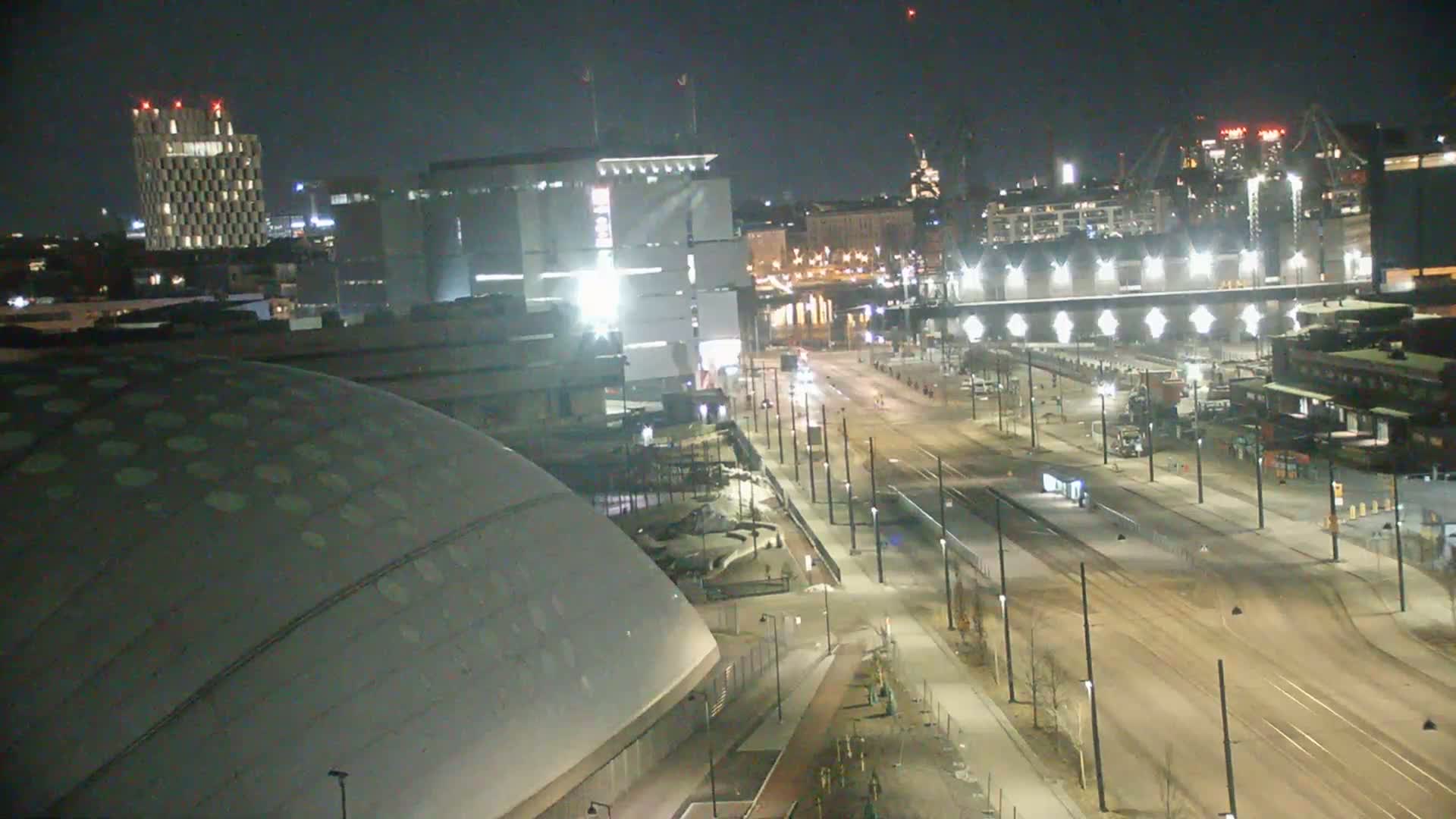 A nighttime, high-angle view of a city street scene with a large domed building and several other structures, including a tall building in the background, under clear skies.