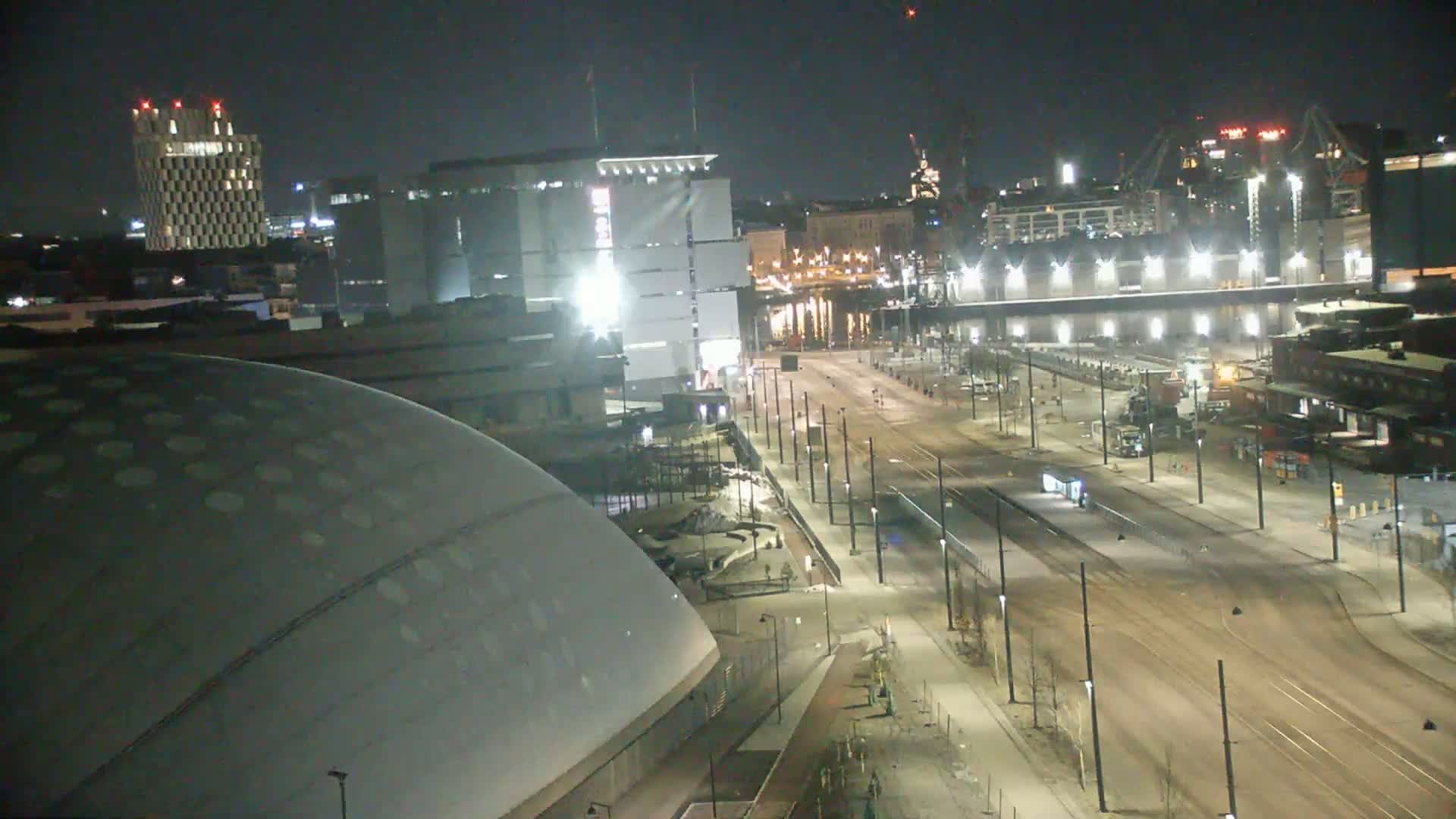 A nighttime view of a city showing a large domed building, several other buildings, and a long, empty street with streetlights and tram tracks.
