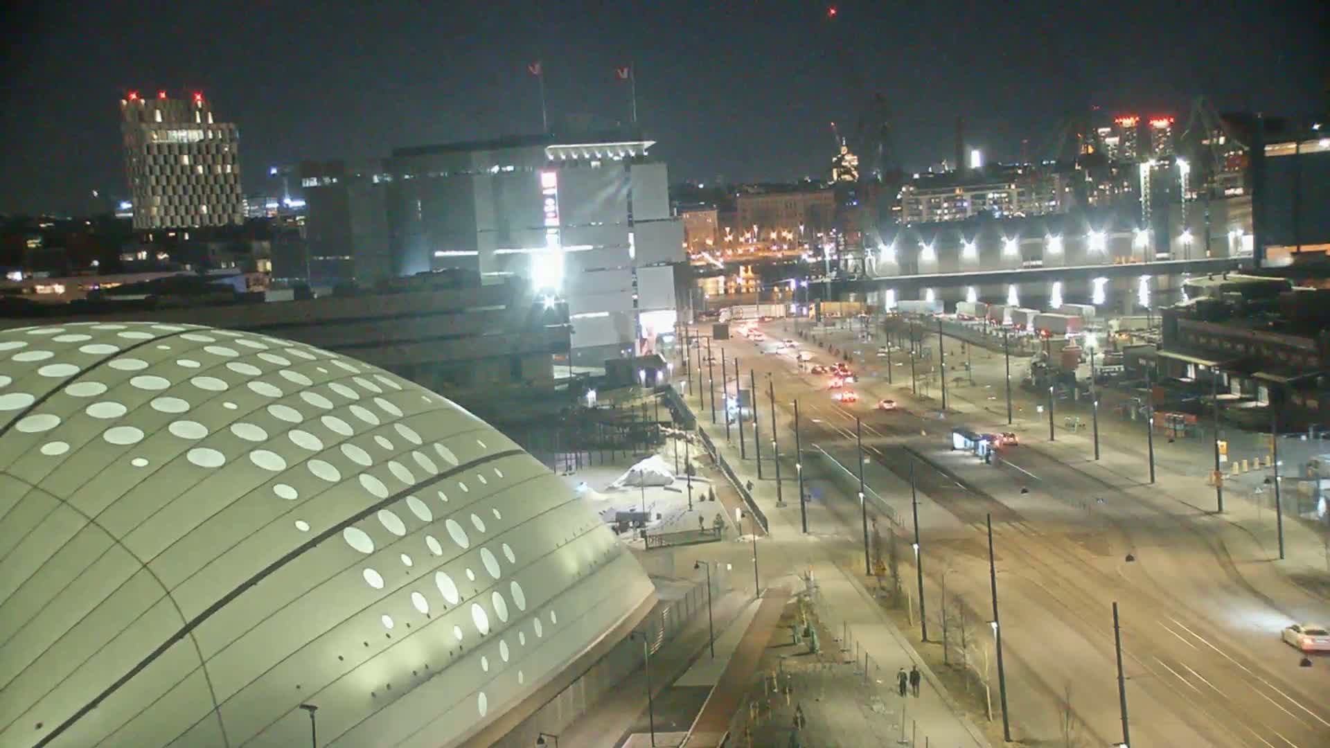 A nighttime, high-angle view of a city street with tram tracks,  buildings including a domed structure with a patterned exterior, and minimal traffic.