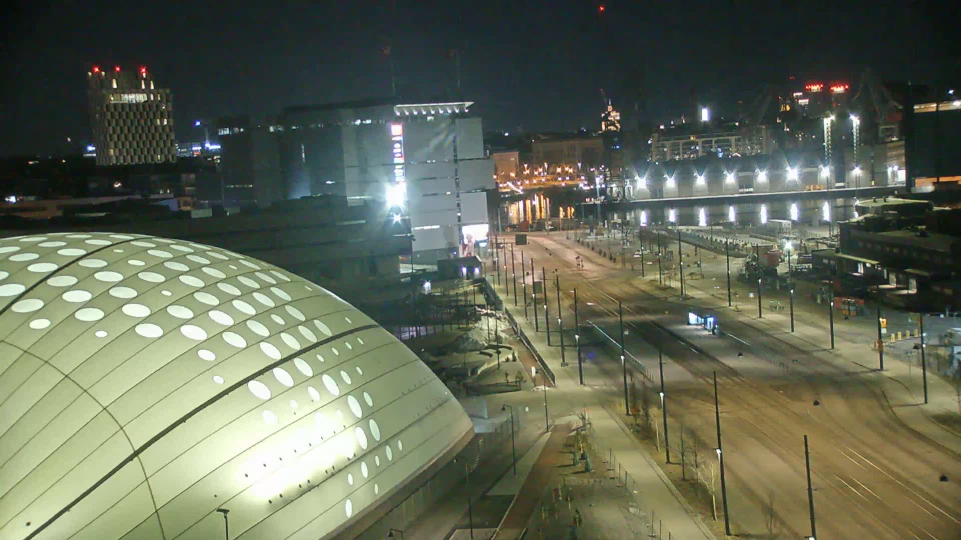 A nighttime view of a city showing a large domed building, a street with tram tracks, and various other buildings under clear skies.