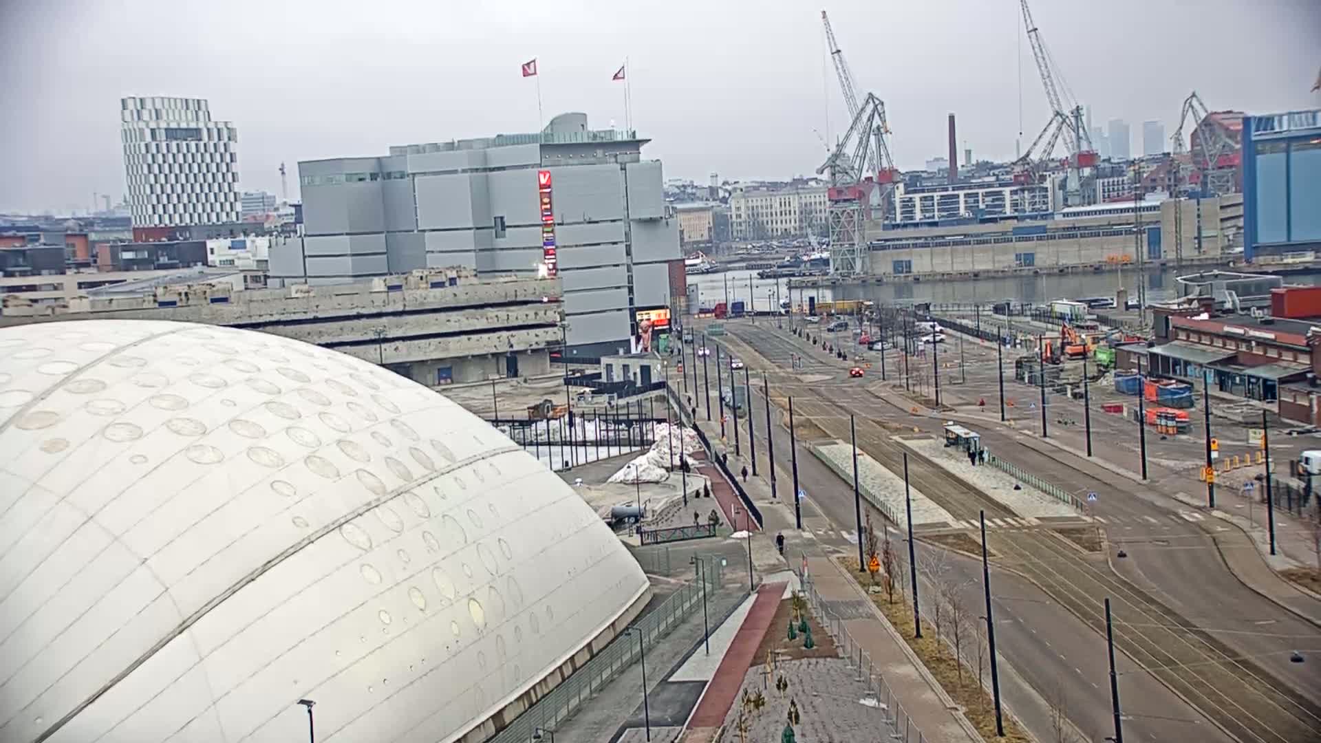 A large white domed building sits next to a wide city street with tram tracks under an overcast sky.