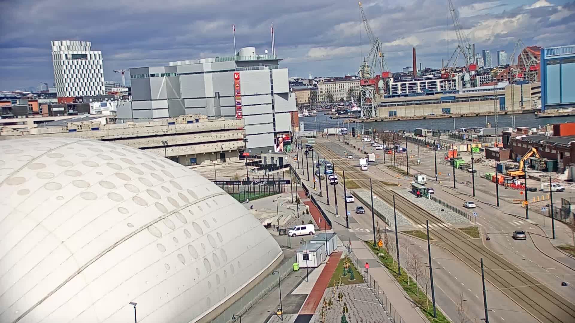 A mostly sunny day shows a large domed building, a city street with tram tracks, a harbor with industrial buildings and cranes, and several high-rise buildings in the background.