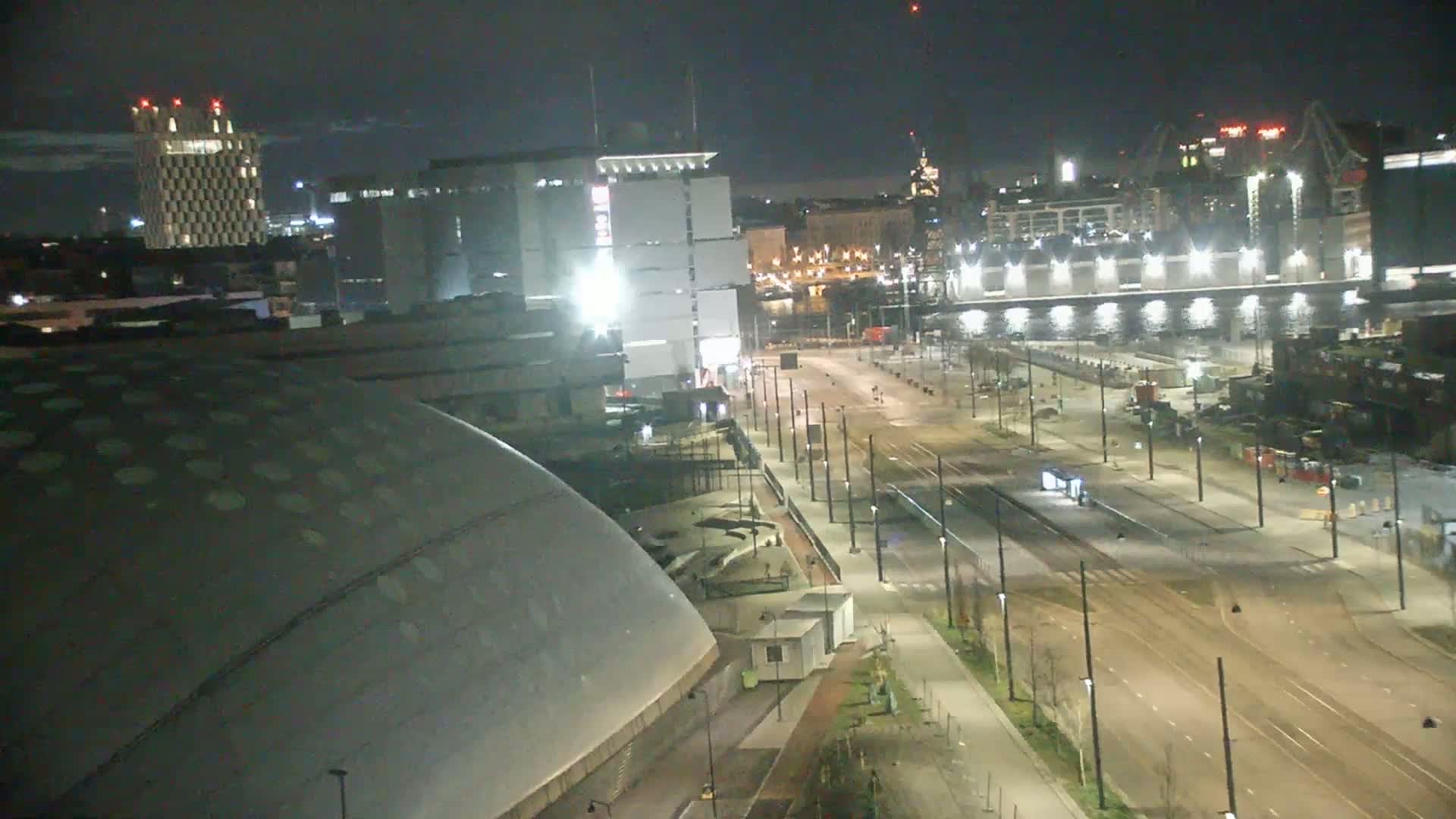 A nighttime, city view shows a large domed building, several other buildings, and a mostly empty street, with lights illuminating the scene.