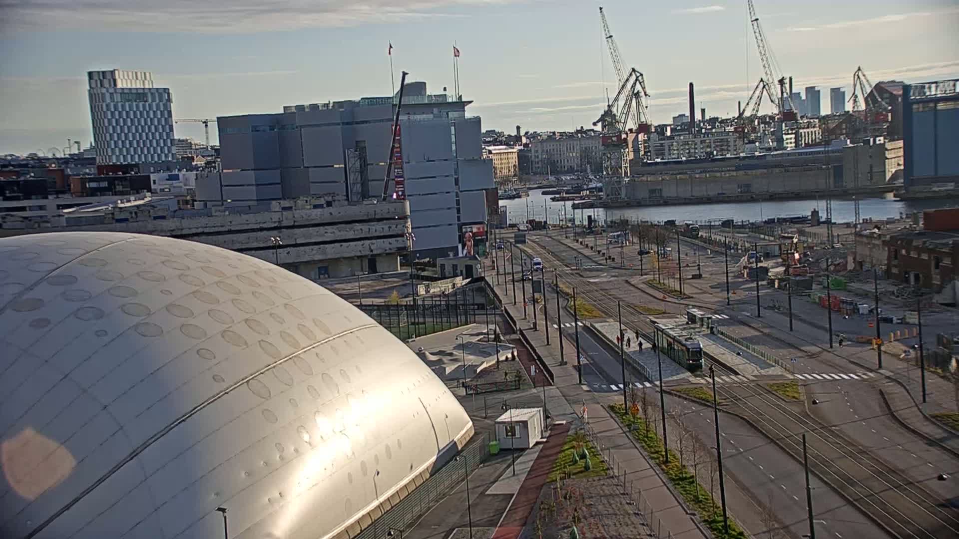 A large, domed building is situated near a waterfront city scene under a partly cloudy sky, with tram lines and construction visible in the foreground.