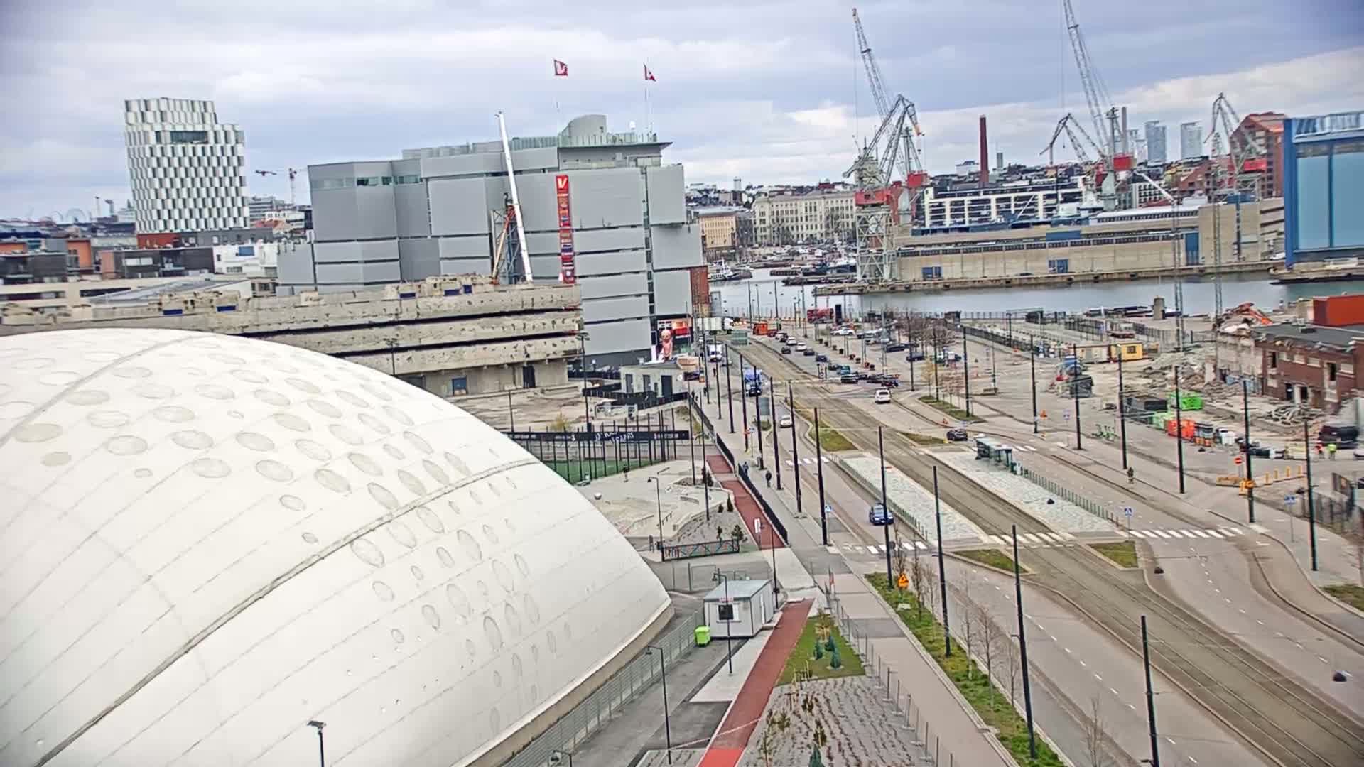 An overcast day reveals a cityscape with a large white dome-shaped building, a road with light traffic, and ongoing construction projects near a harbor.