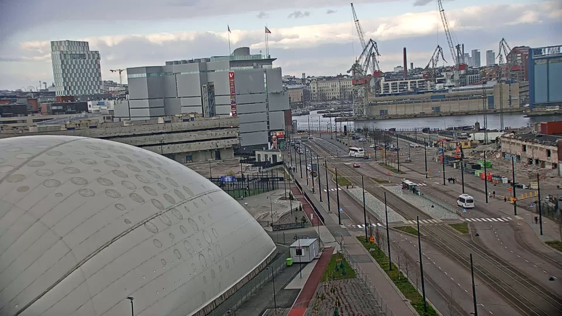 An overcast day reveals a cityscape with a large domed building in the foreground, a street with tram tracks running through it, a body of water, and construction cranes in the background.