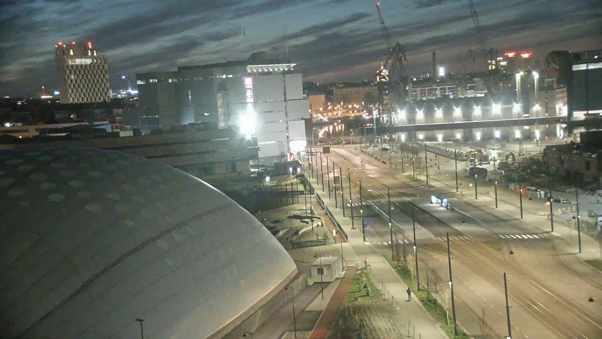 A nighttime view of a city streetscape shows a large domed building, several other buildings, and empty streets under a partly cloudy sky.