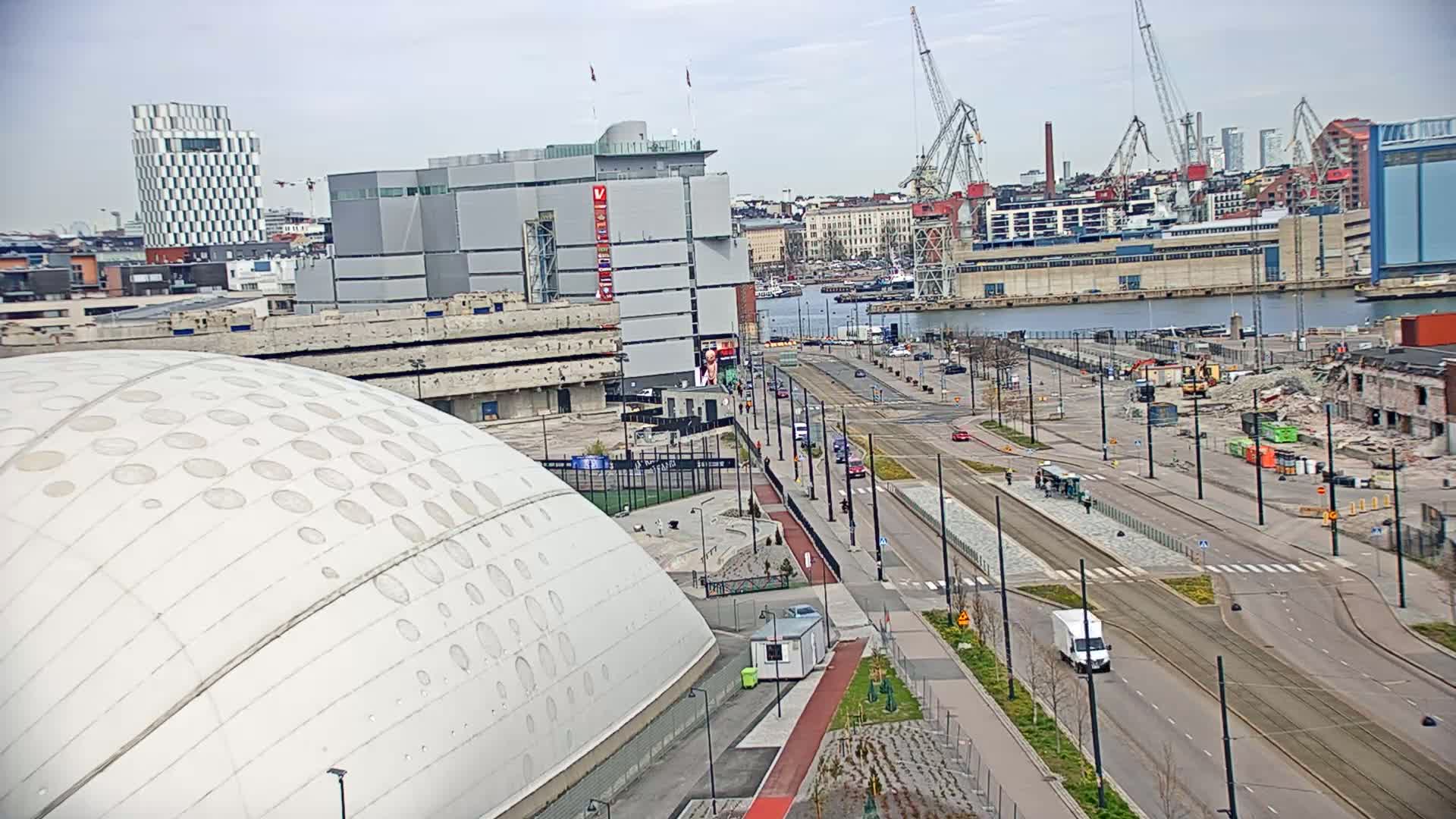 A large domed building is seen in the foreground, with a city street and harbor in the background under a partly cloudy sky.