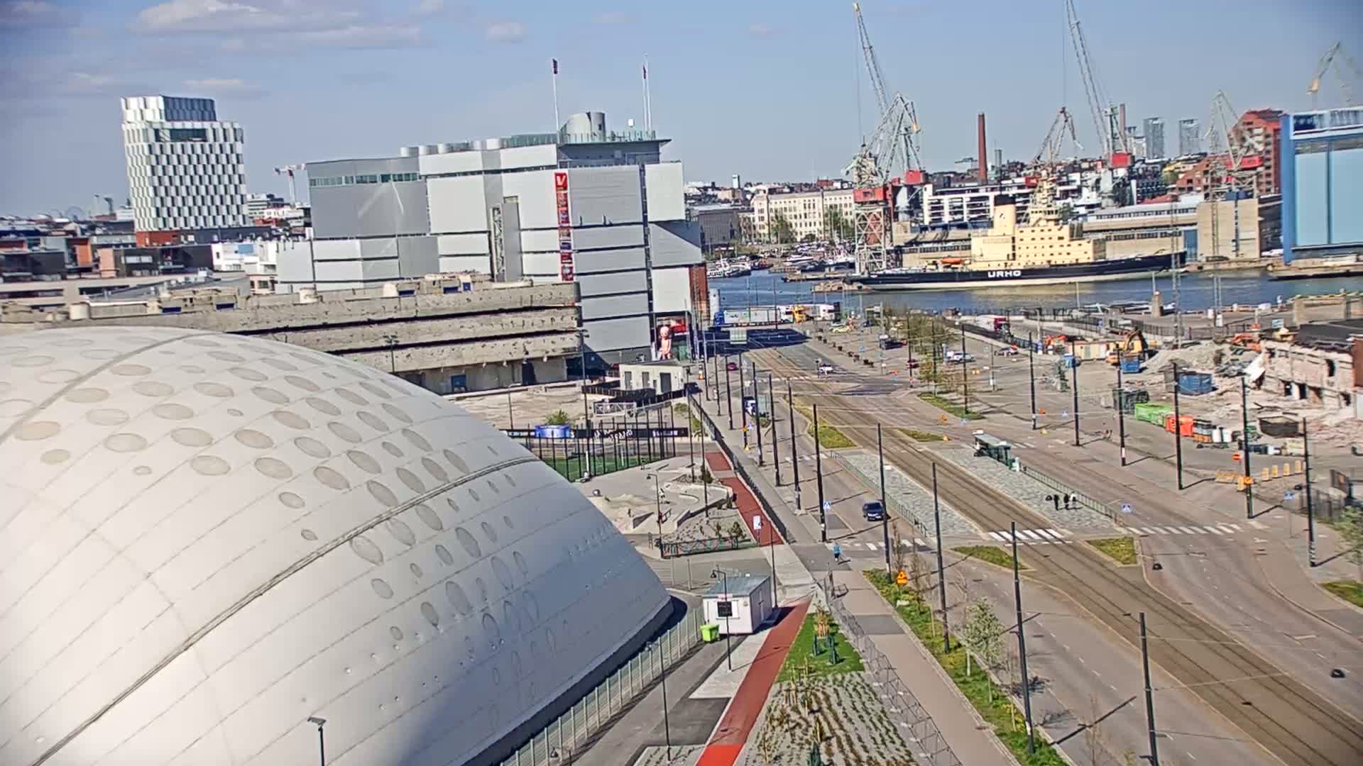 A partly sunny day reveals a cityscape featuring a large domed building, modern architecture, a harbor with a ship, and a street with tram lines, all under construction in areas.