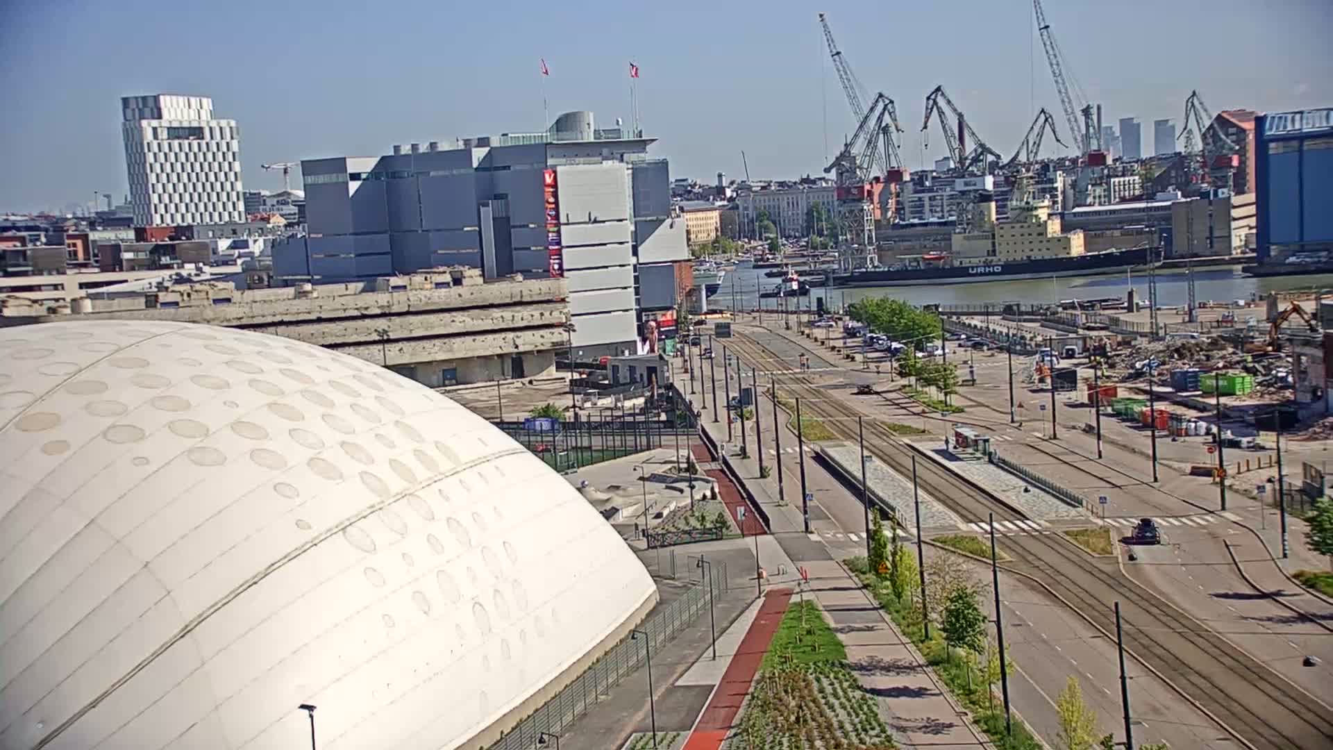A mostly sunny day reveals a cityscape with a large white domed building, a harbor with cranes and ships, and a tram line running through a developing area.