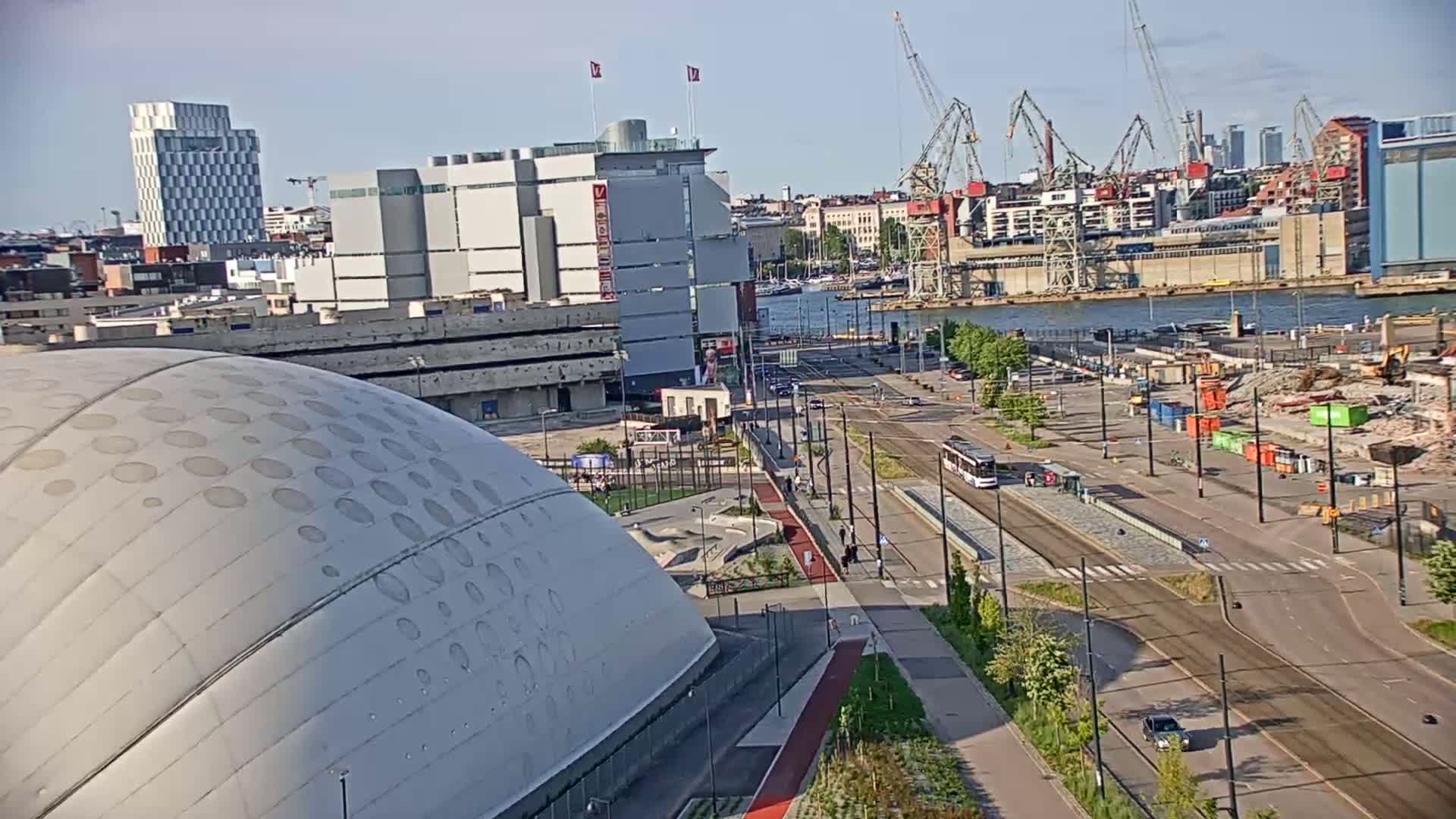 A large domed building is situated near a waterfront city scene under a clear sky, with a roadway, trams, and construction visible in the background.