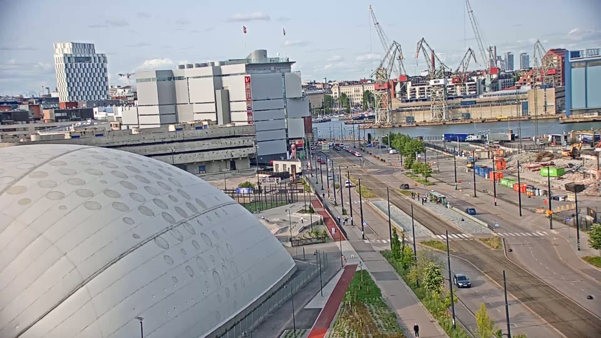 A mostly sunny day reveals a cityscape with a large domed building, a waterfront with cranes, and a street scene with pedestrians and trams.