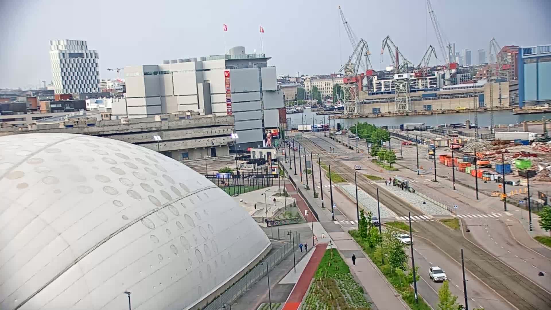 A large, domed building sits in the foreground of a city scene under an overcast sky, with a harbor, cranes, and buildings in the background.