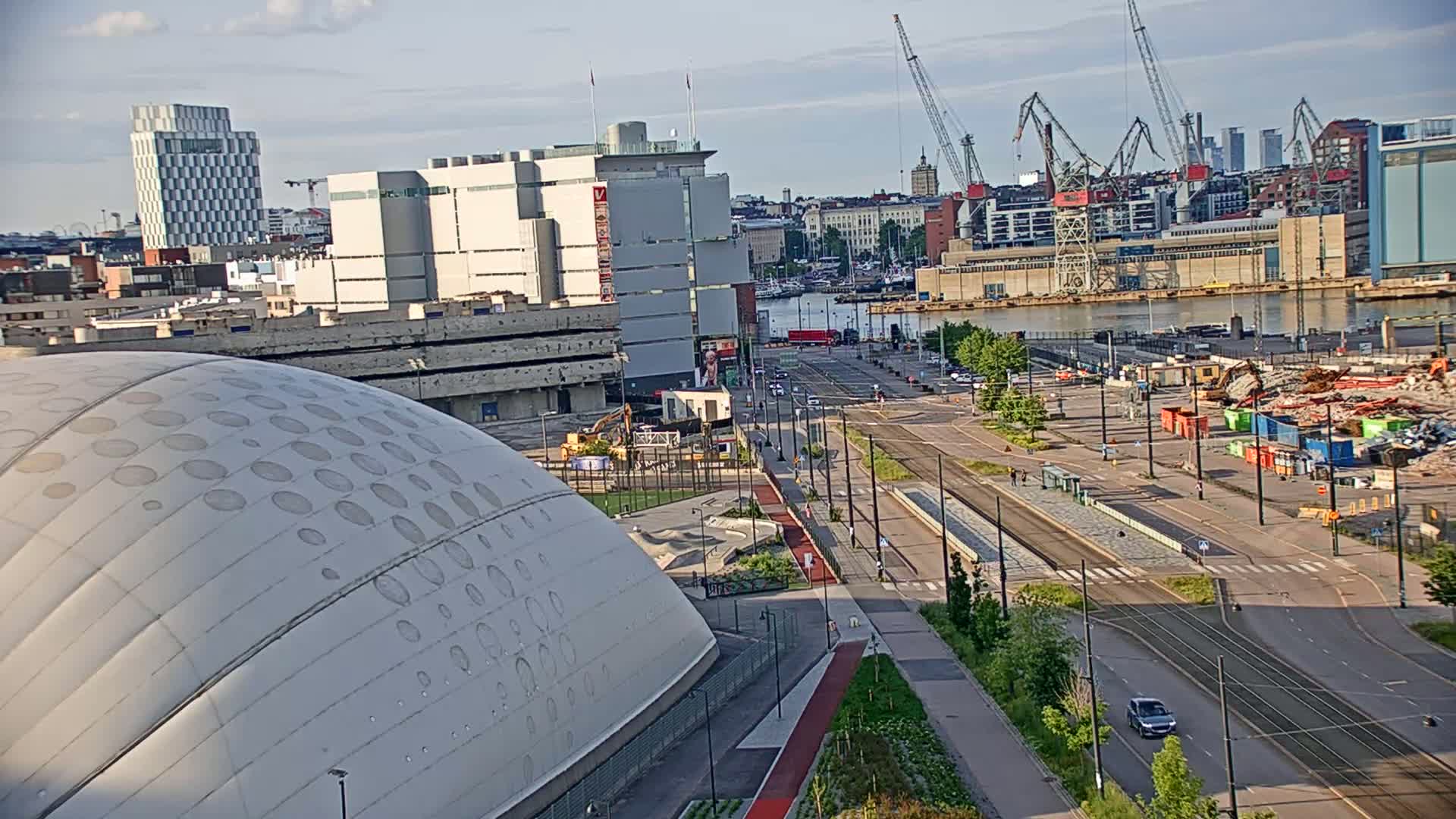 A high-angle view shows a domed building and a city scene under a partly cloudy sky, with construction and cranes visible near a body of water.