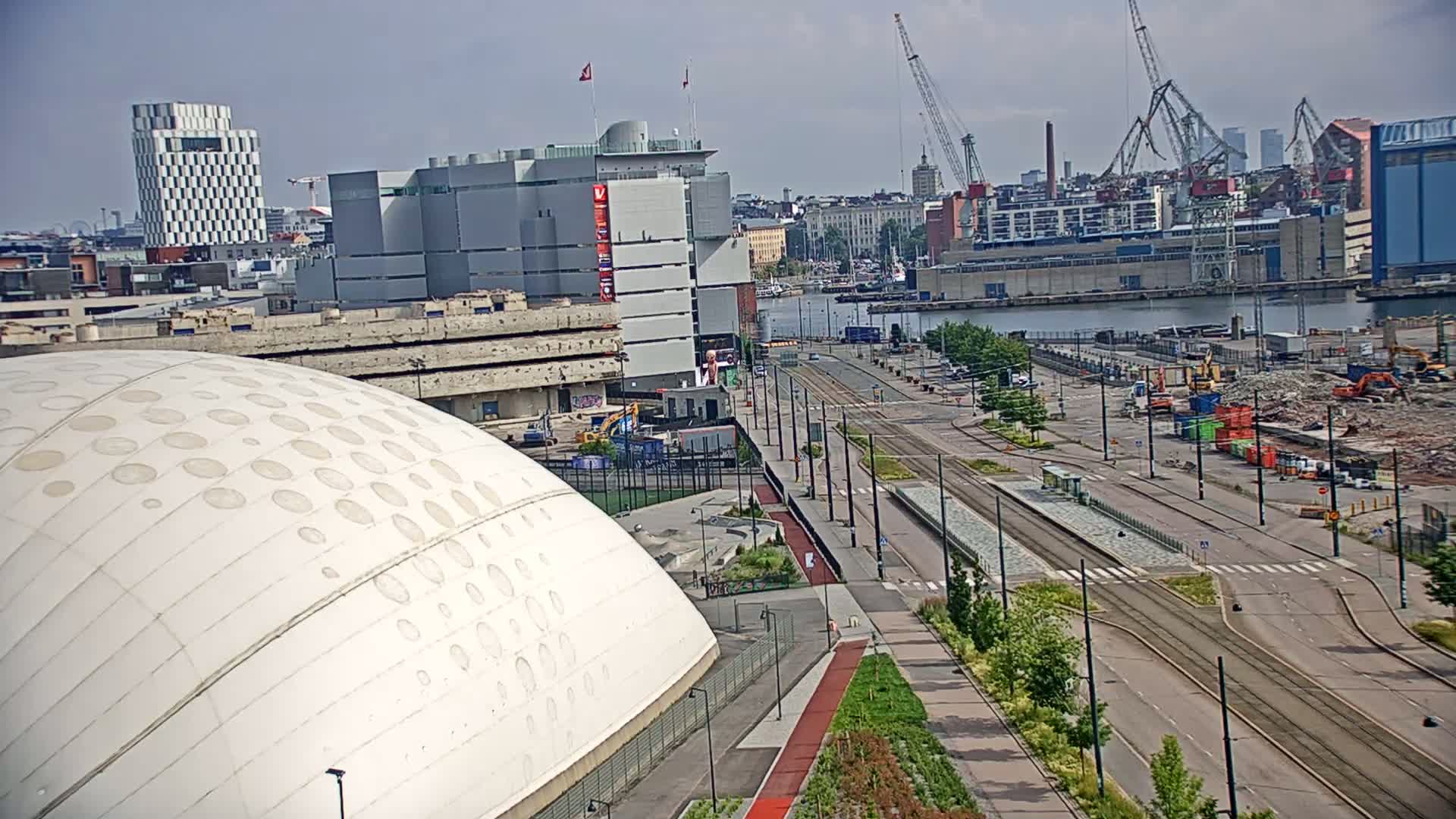 A large white domed building sits in the foreground, overlooking a city harbor with tram tracks and construction sites on a sunny day.