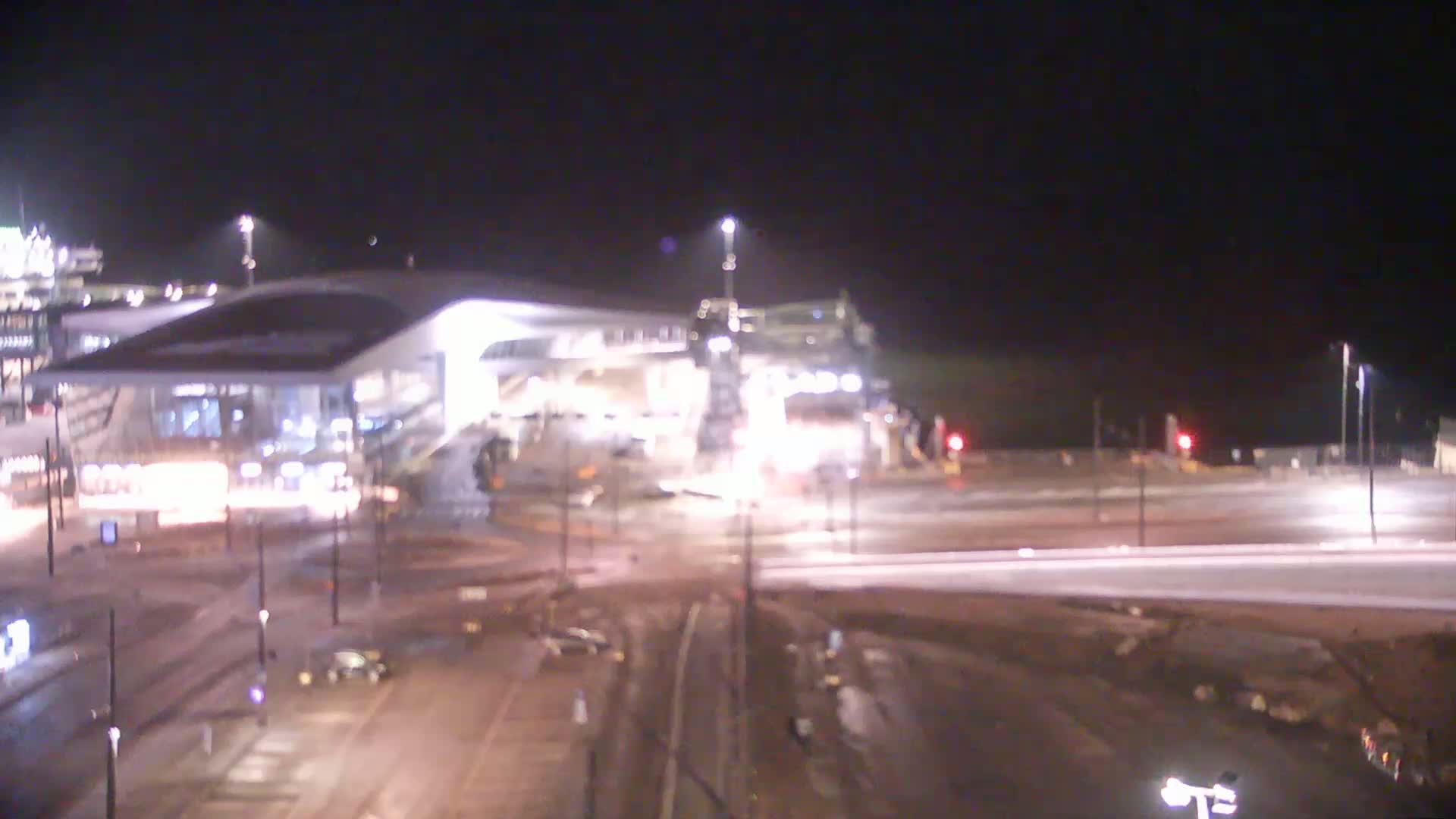 A brightly lit, modern building at night with surrounding roadways and some vehicle traffic under dark, clear skies.