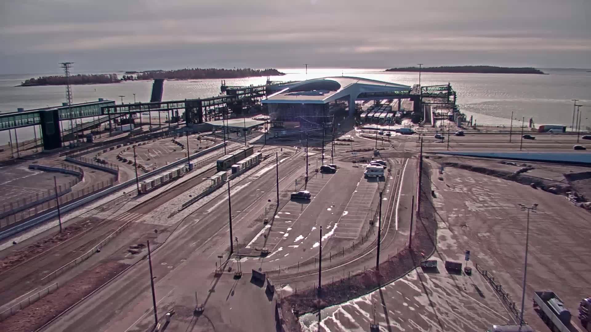 An aerial view shows a ferry terminal with trains and cars, under a partly cloudy sky.
