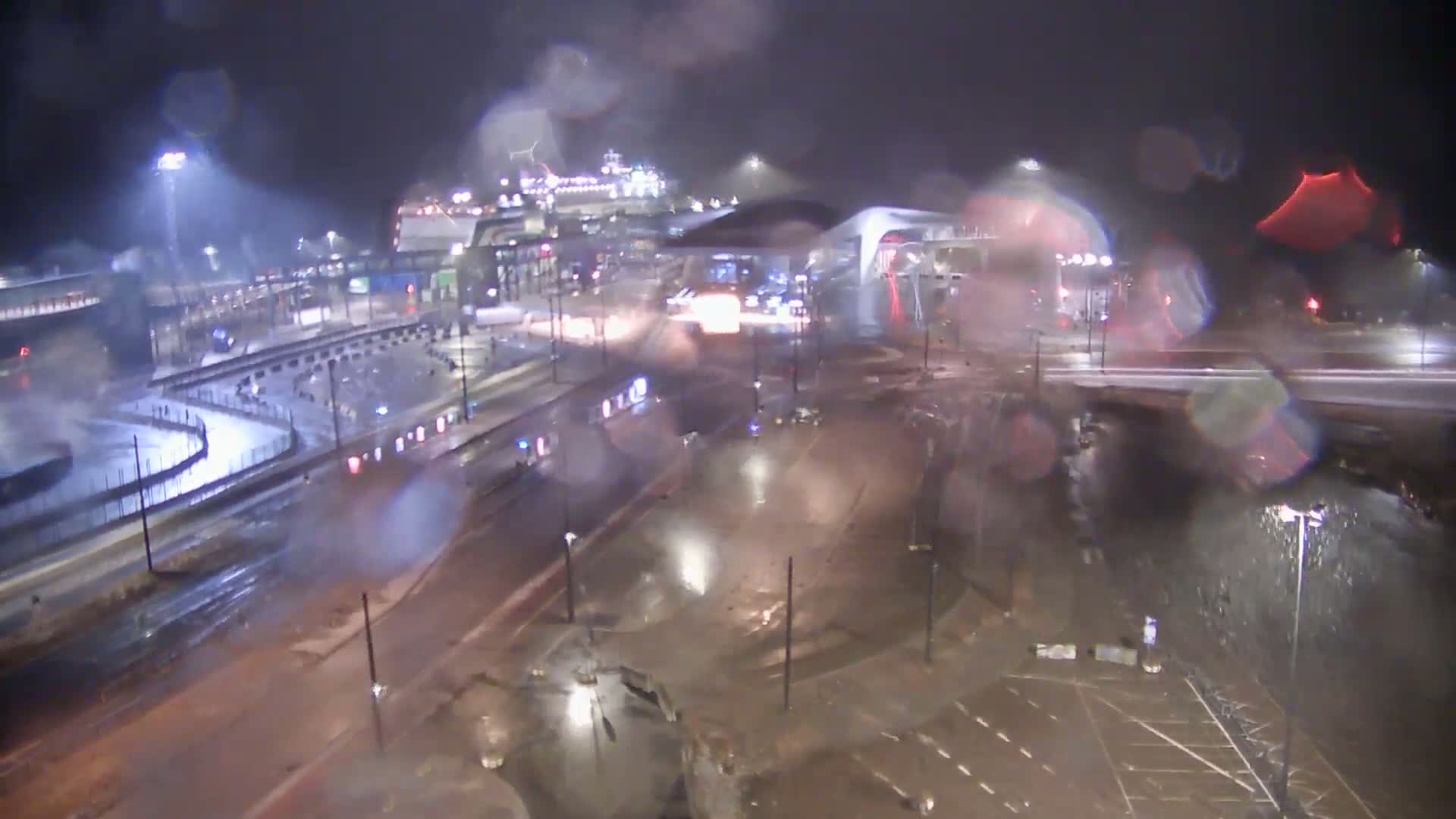 A ferry terminal at night in heavy rain, with wet roads and a large ferry docked nearby.
