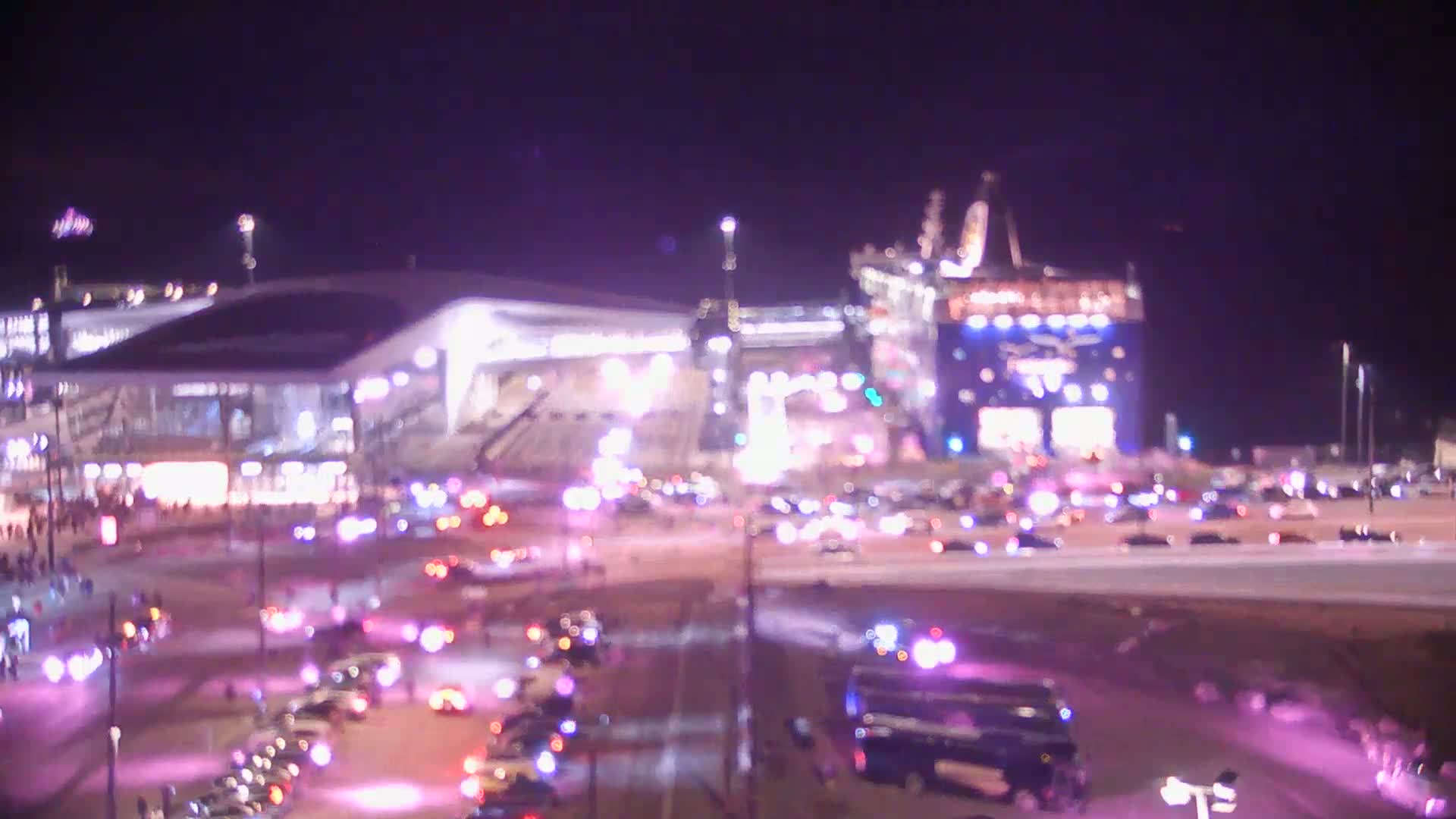 A brightly lit stadium and surrounding area at night are filled with numerous vehicles, many of which appear to be emergency vehicles, under a dark sky.