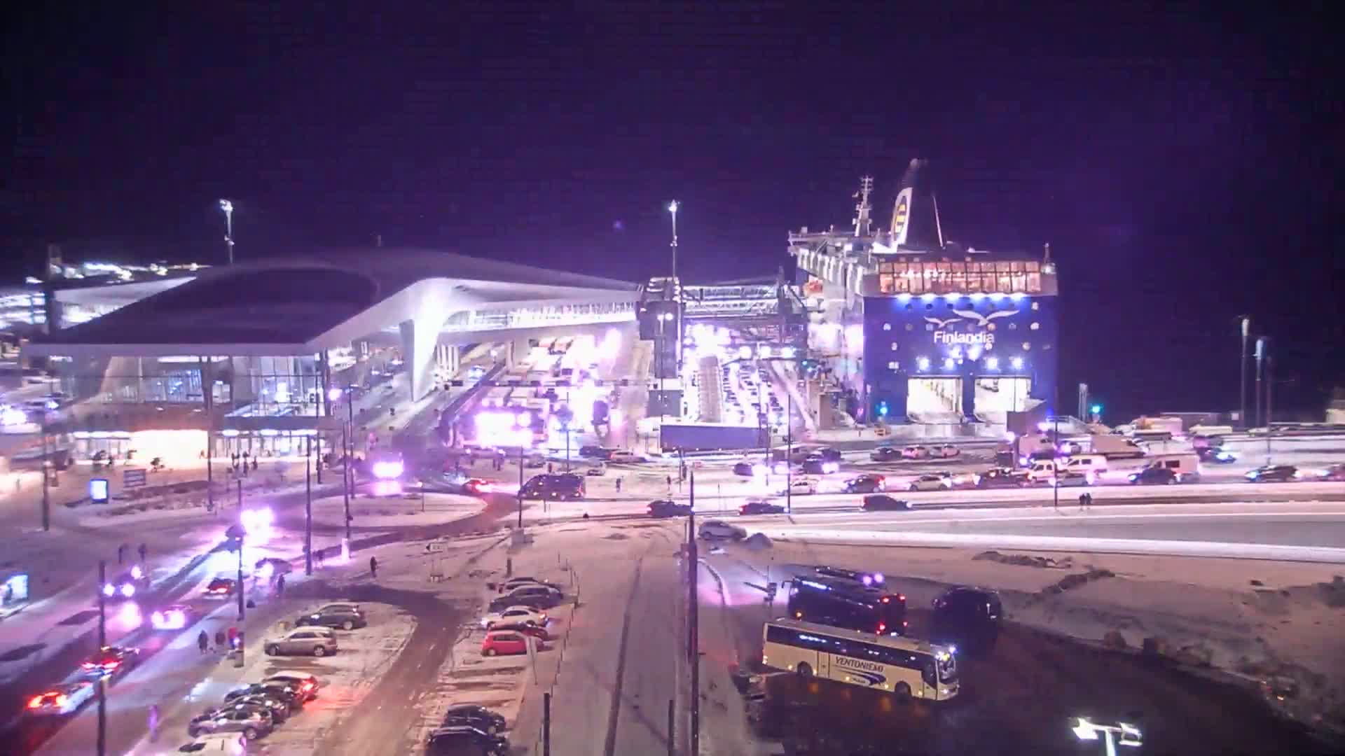 A large ferry is docked at a terminal in a snowy area at night, surrounded by numerous emergency vehicles and cars.