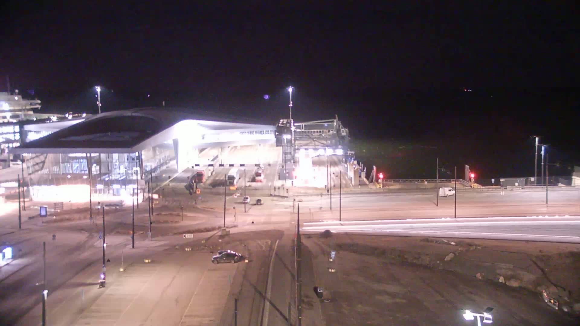 A brightly lit modern ferry terminal at night, with some construction still visible, is shown under dark, clear skies.