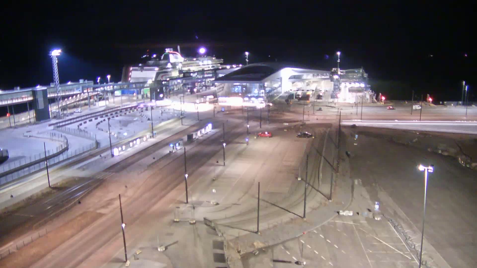 A nighttime, aerial view of a ferry terminal with a large cruise ship docked, surrounded by empty roadways and parking lots.