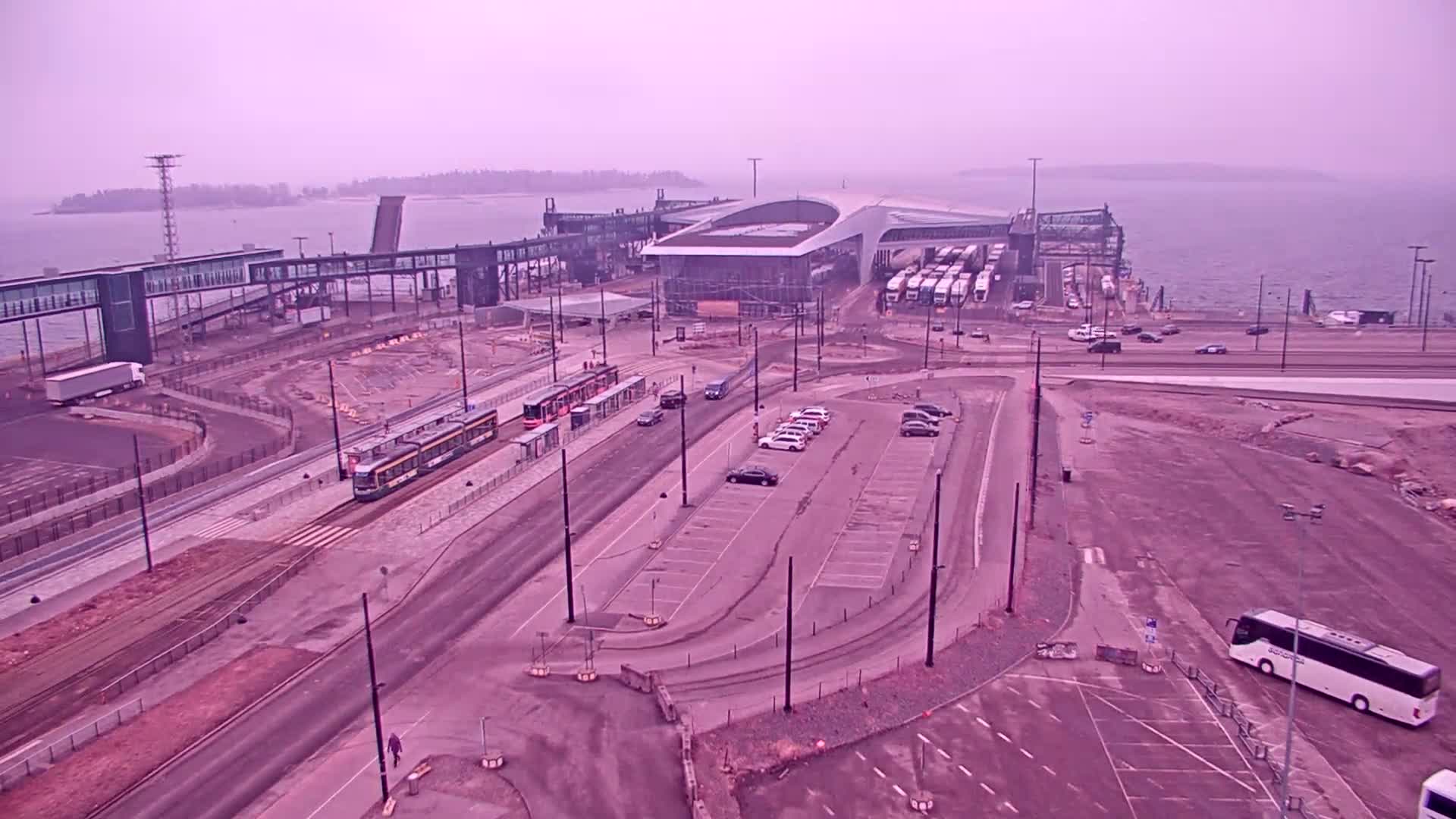 An aerial view shows a ferry terminal with trams, cars, and a bus parked nearby on an overcast day.