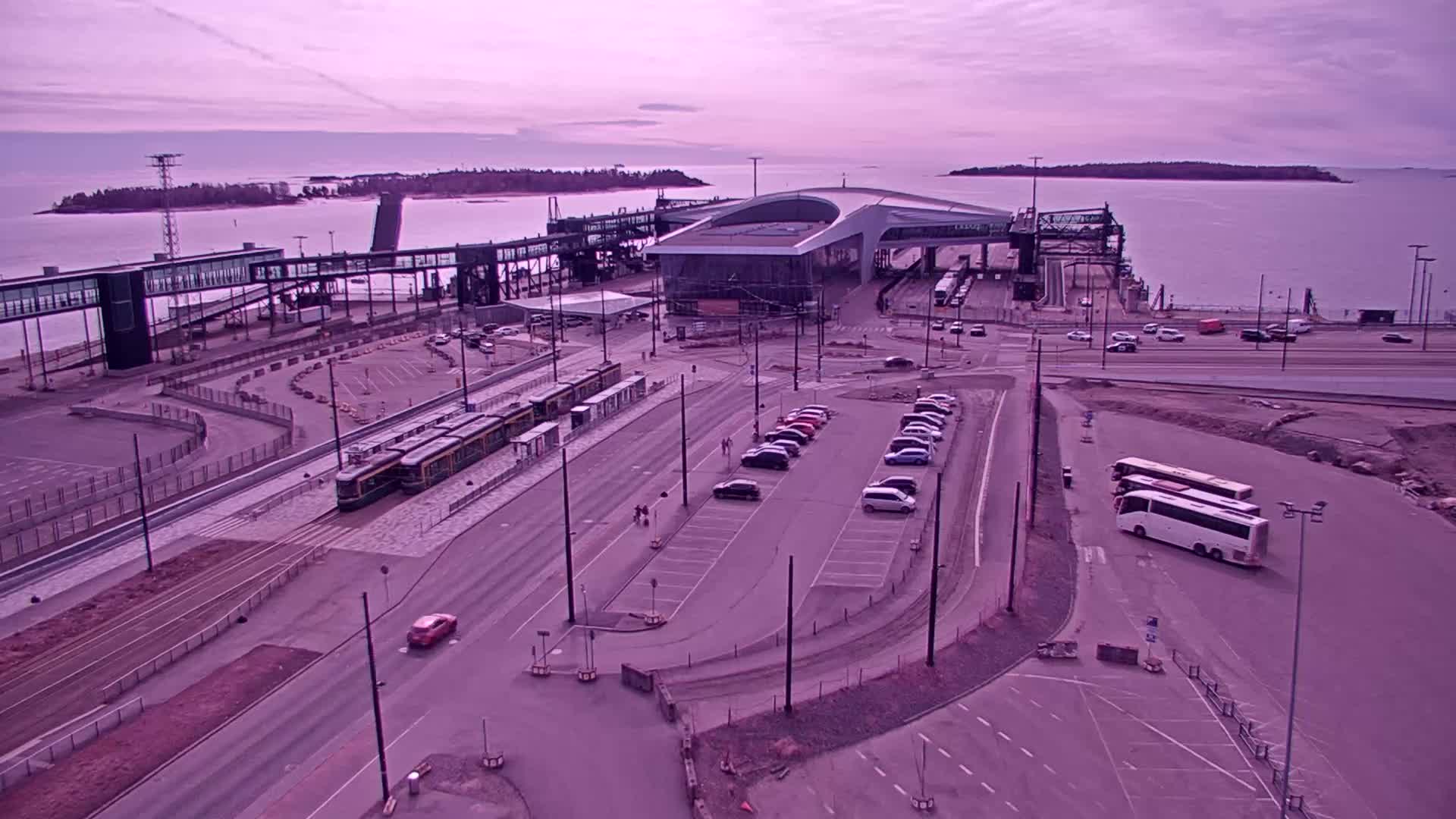 An aerial view of a ferry terminal with trams, cars, and buses parked under a dusky sky.