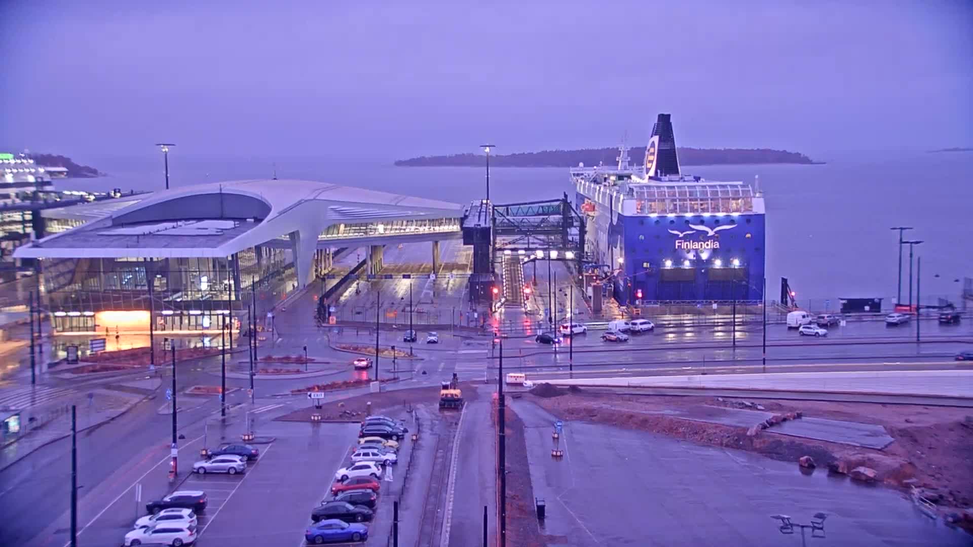 A large ferry is docked at a terminal building in the rain under an overcast sky.