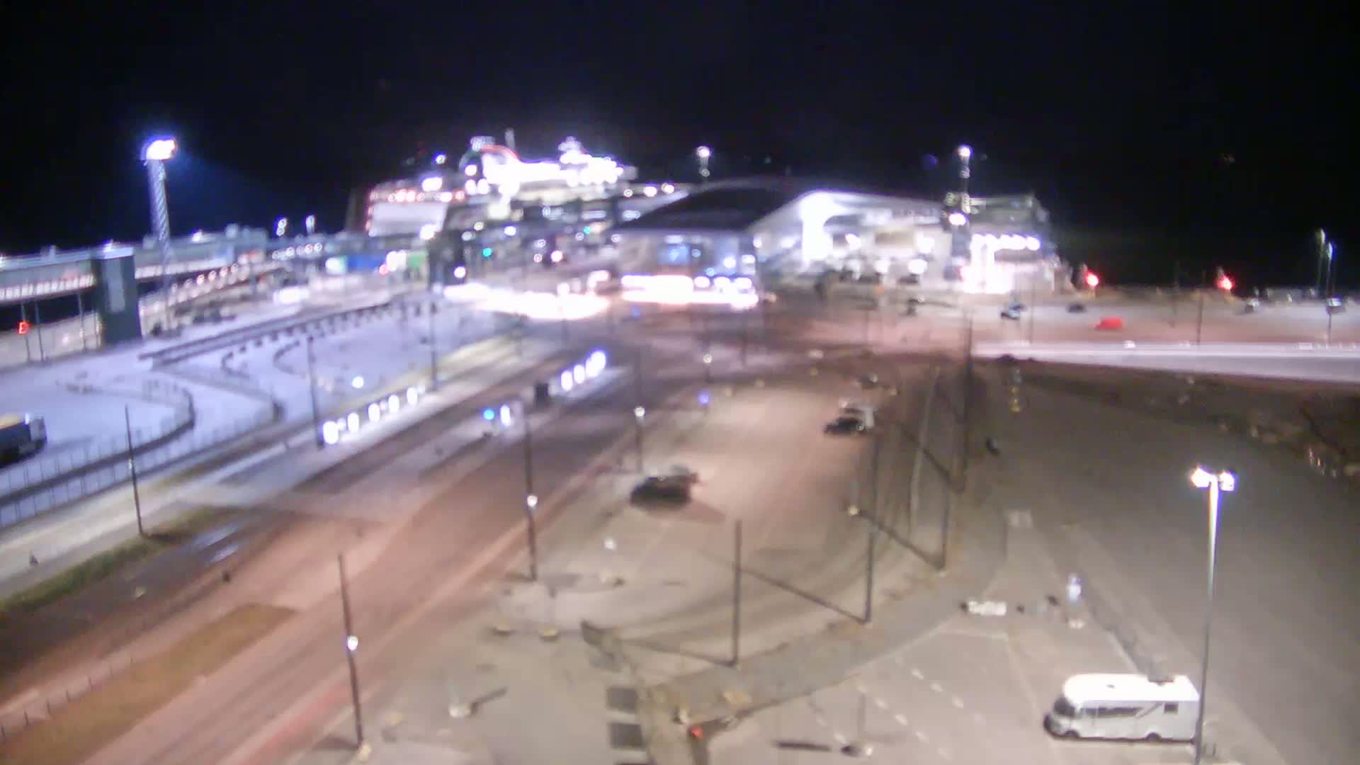 At night, a cruise ship is docked at a terminal, with roads and parking lots surrounding it.