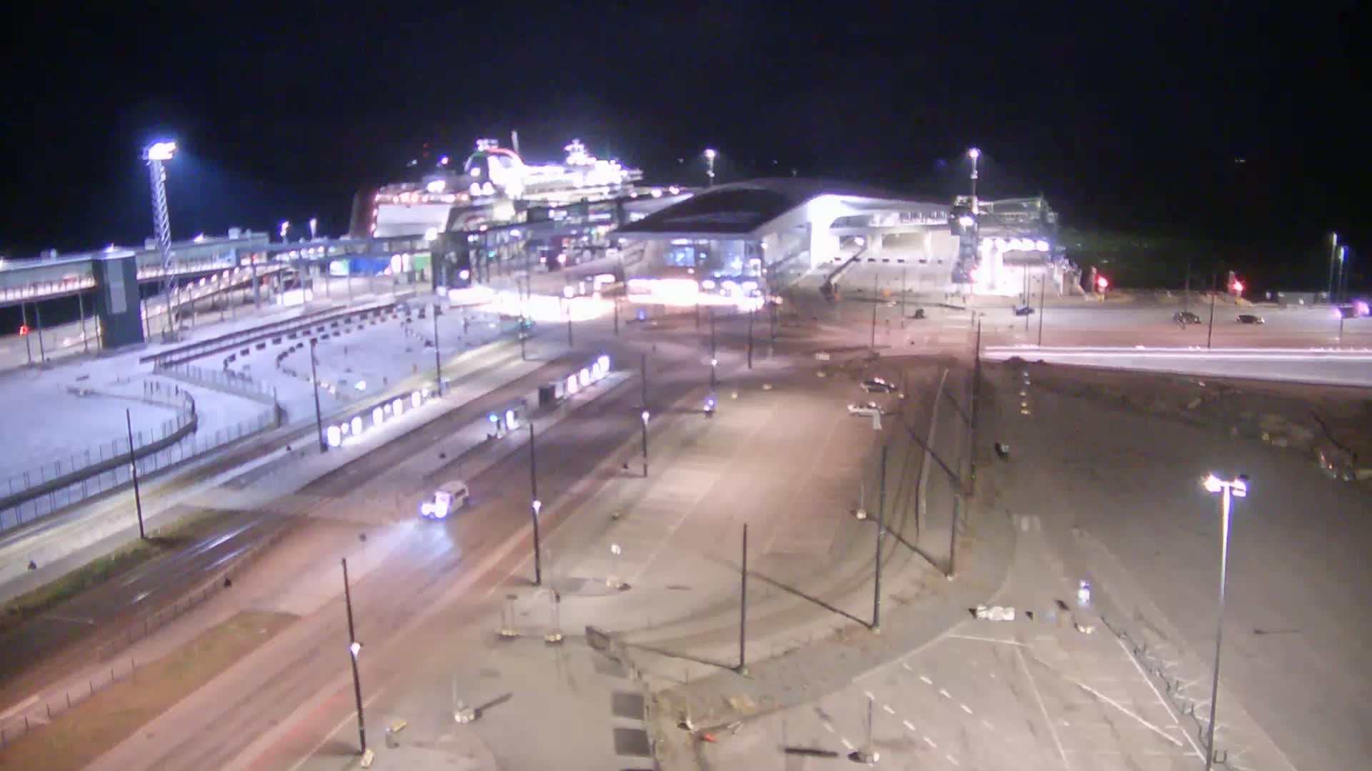 A large ferry is docked at a terminal at night, with roadways and parking areas visible around it under well-lit conditions.