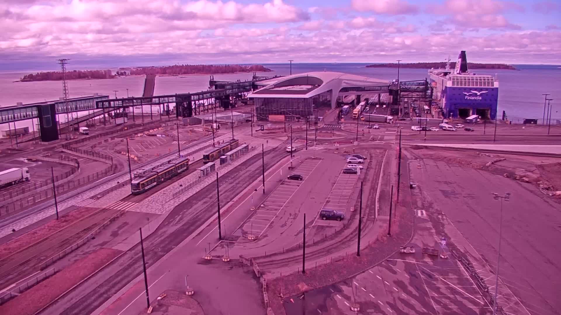 A ferry is docked at a terminal with trams nearby under a cloudy, purplish sky.