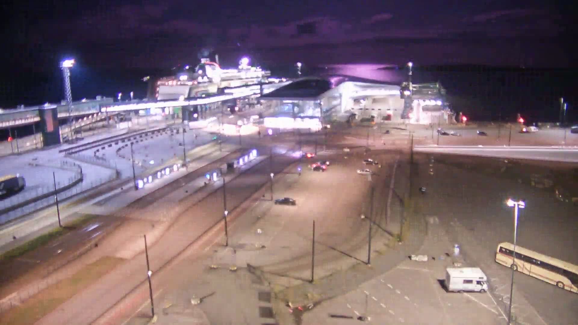 A large cruise ship is docked at a terminal at night under a dark, possibly cloudy sky.