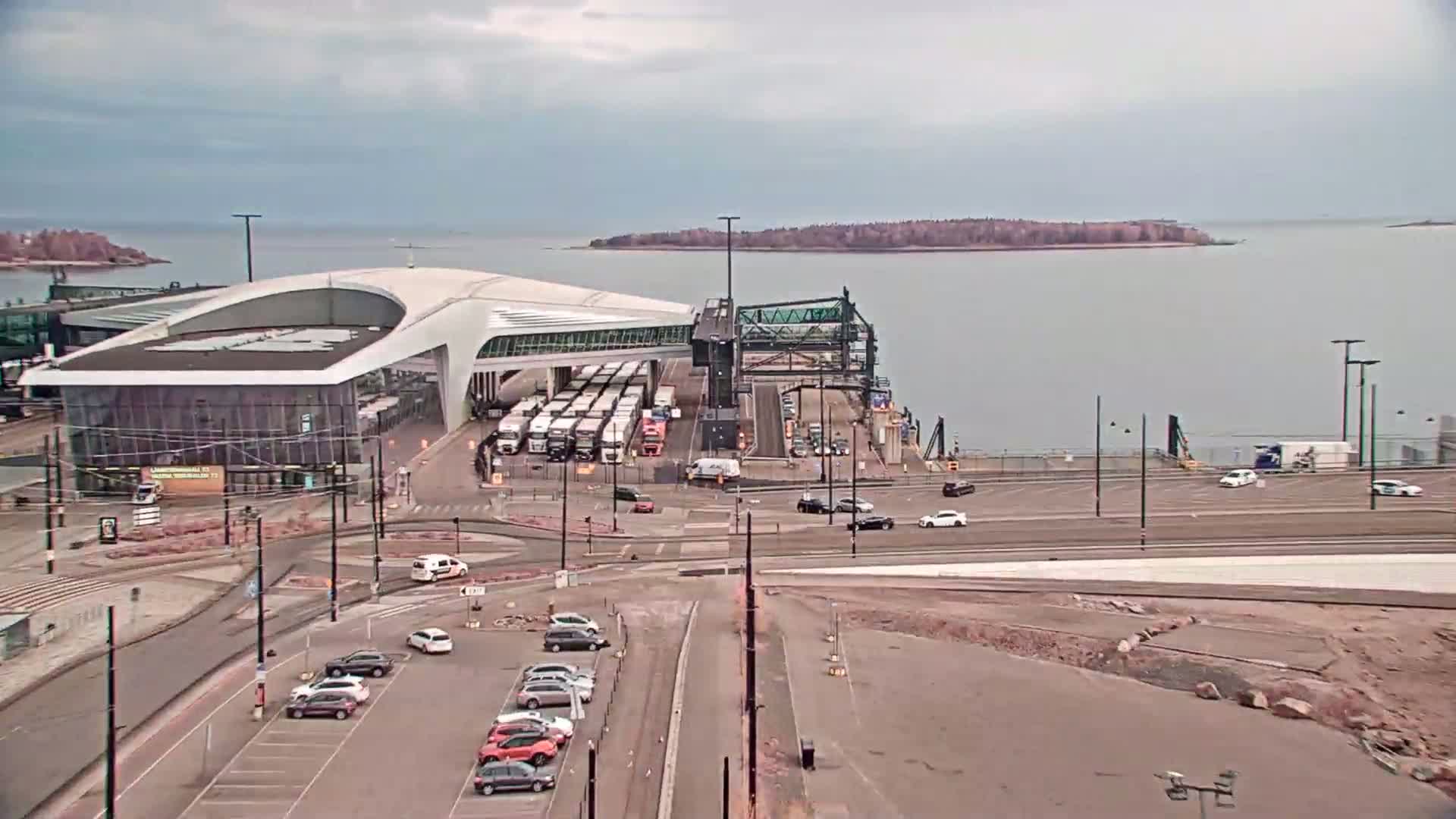 A ferry terminal with numerous trucks and cars, situated on a body of water under an overcast sky.