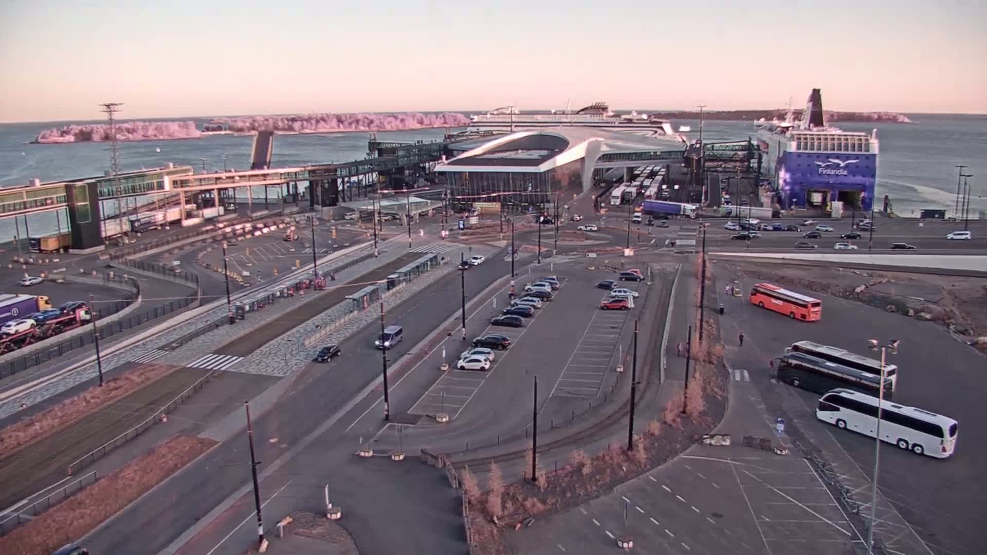An aerial view of a ferry terminal with several cars parked in lots and buses, under a dusky sky.