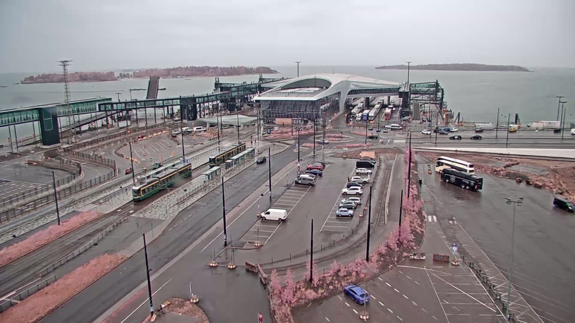 A ferry terminal with trams and buses, a parking lot, and a body of water under an overcast sky.