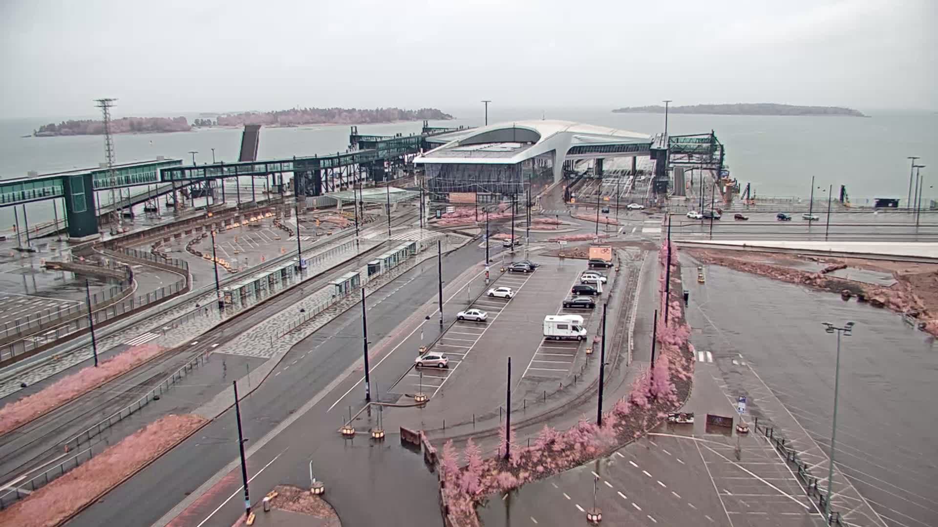A ferry terminal with a modern building and connecting walkways, surrounded by parking lots and roadways, is partially flooded under an overcast sky.