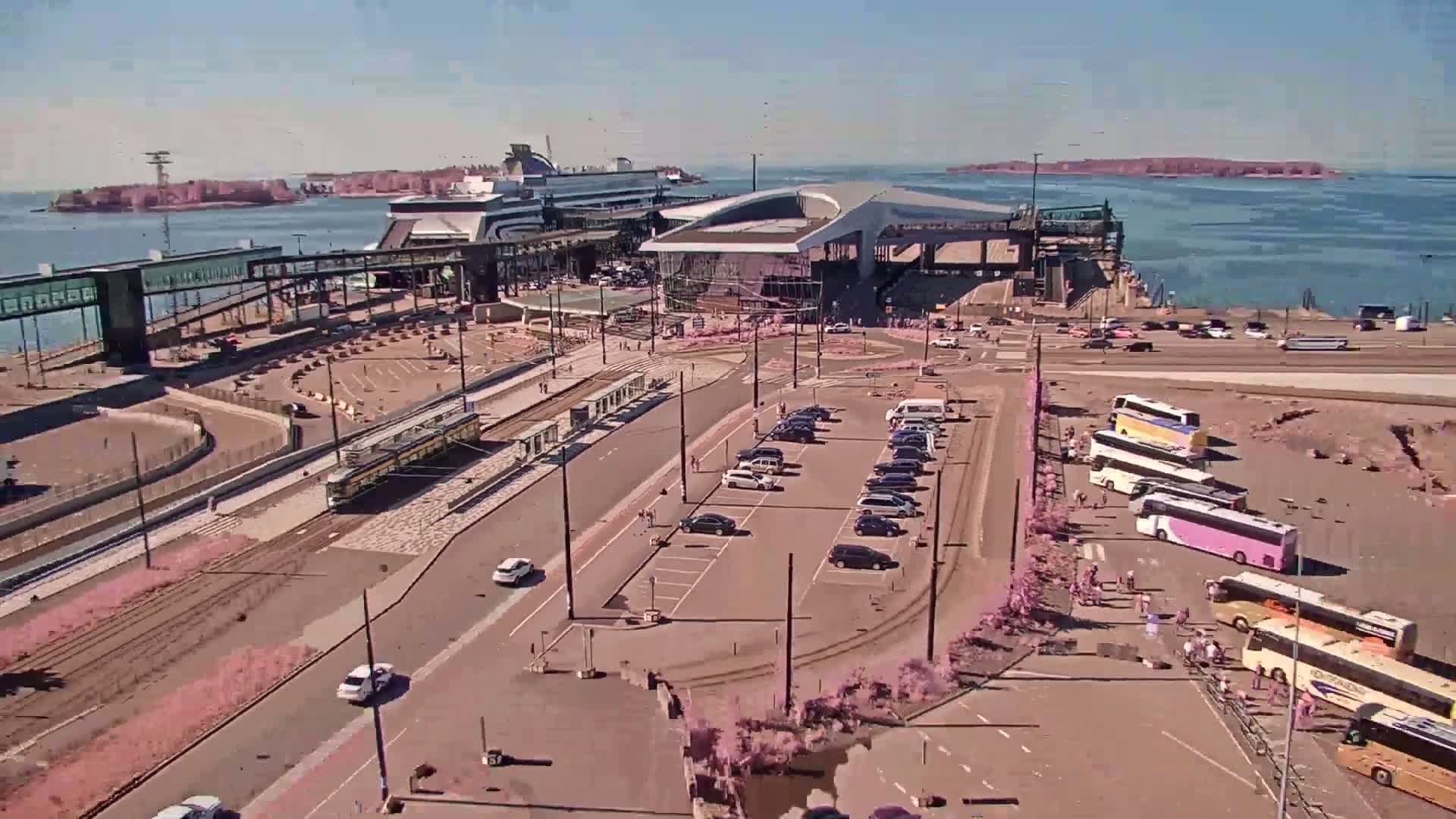 An aerial view of a ferry terminal at dusk, with cars parked nearby and a calm body of water visible beyond.