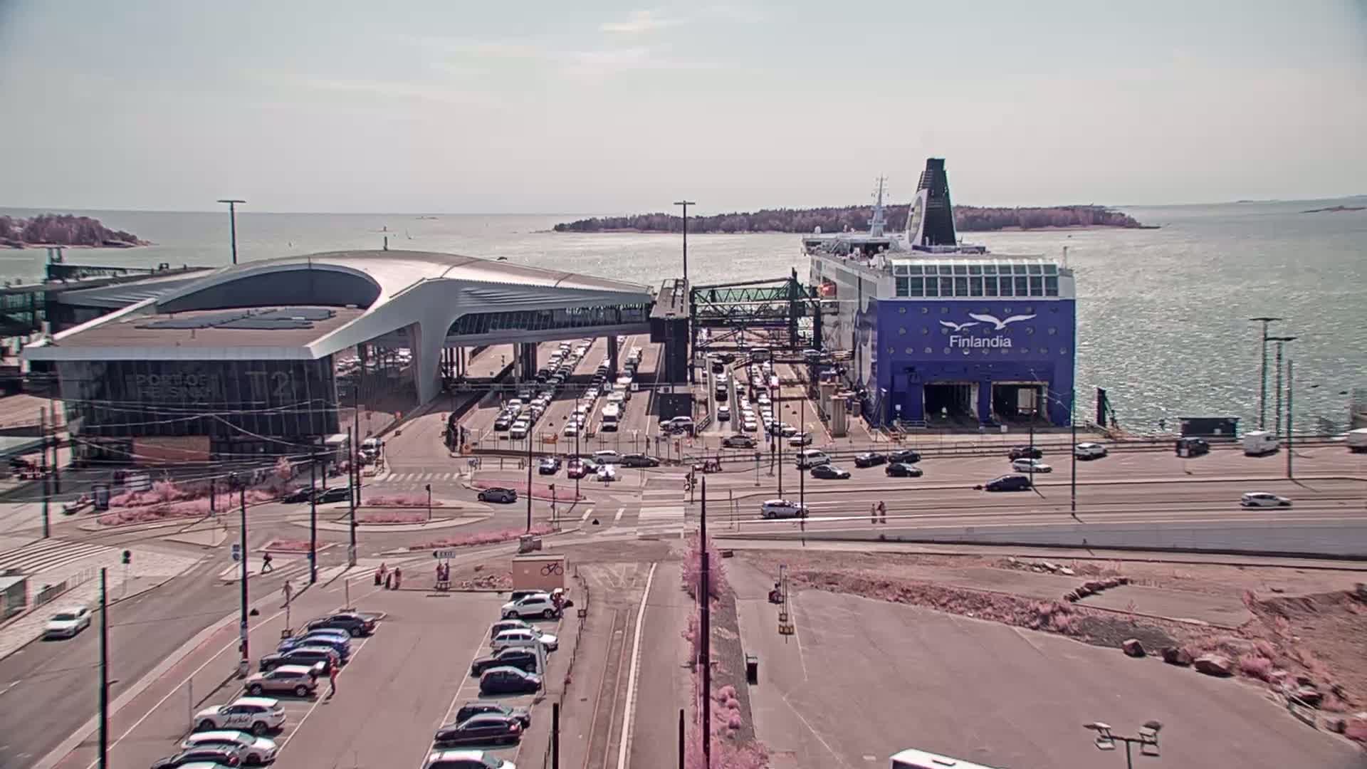 A large ferry is docked at a terminal, surrounded by cars in a sunny, clear day.