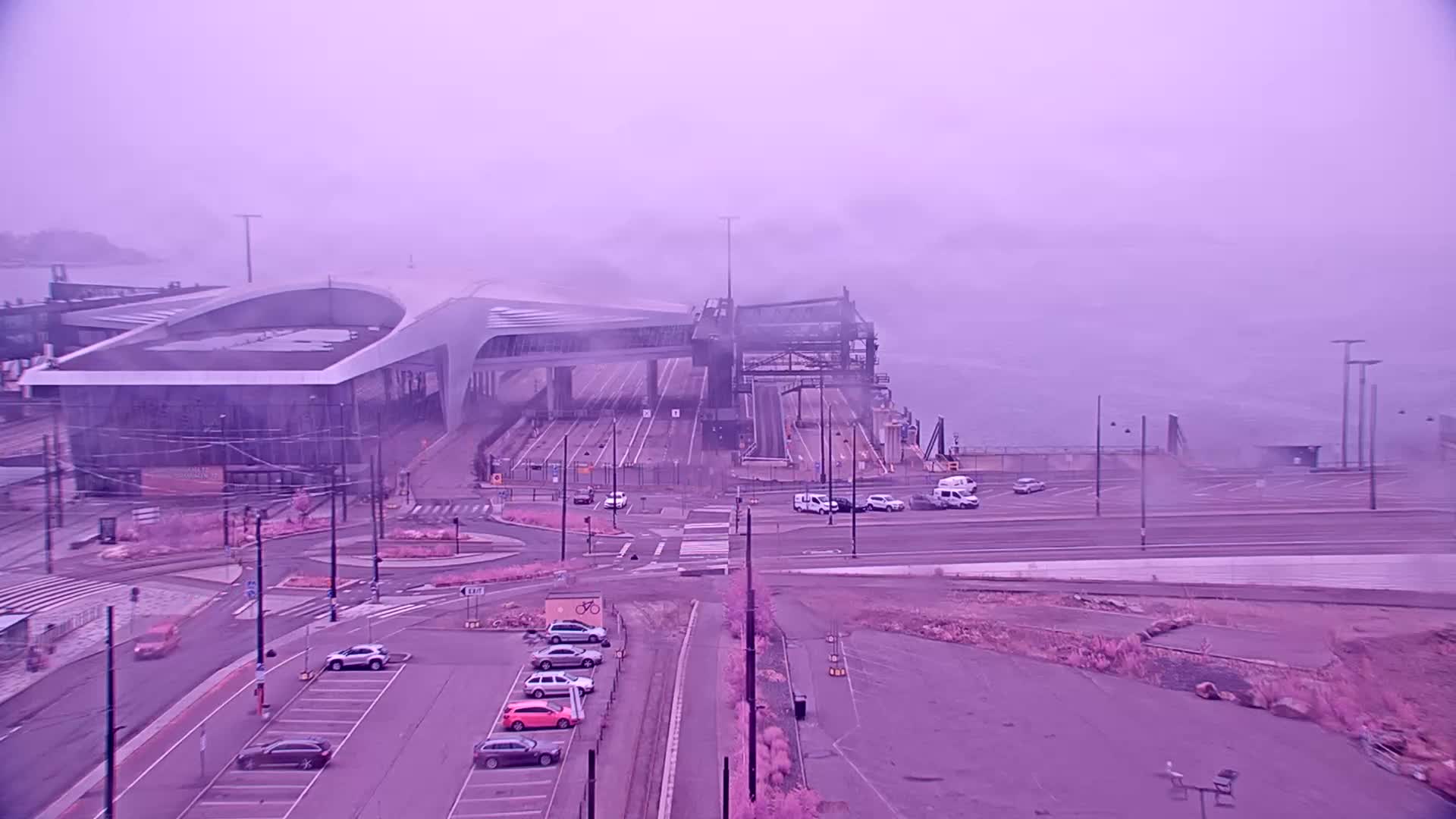 A ferry terminal with a modern building and several vehicles is visible in foggy conditions.