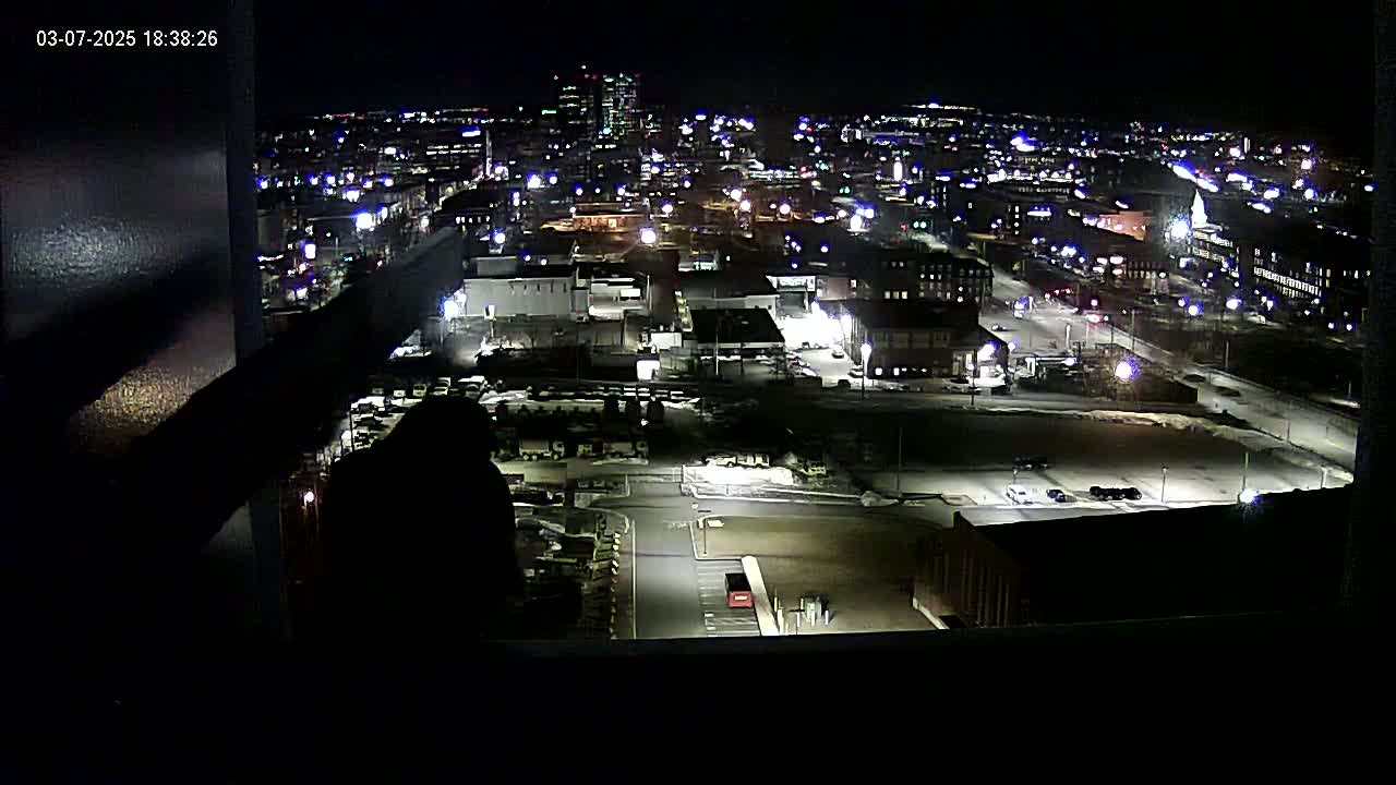 A nighttime aerial view of a city's industrial area, illuminated by streetlights and building lights, with snow or ice visible on the ground.