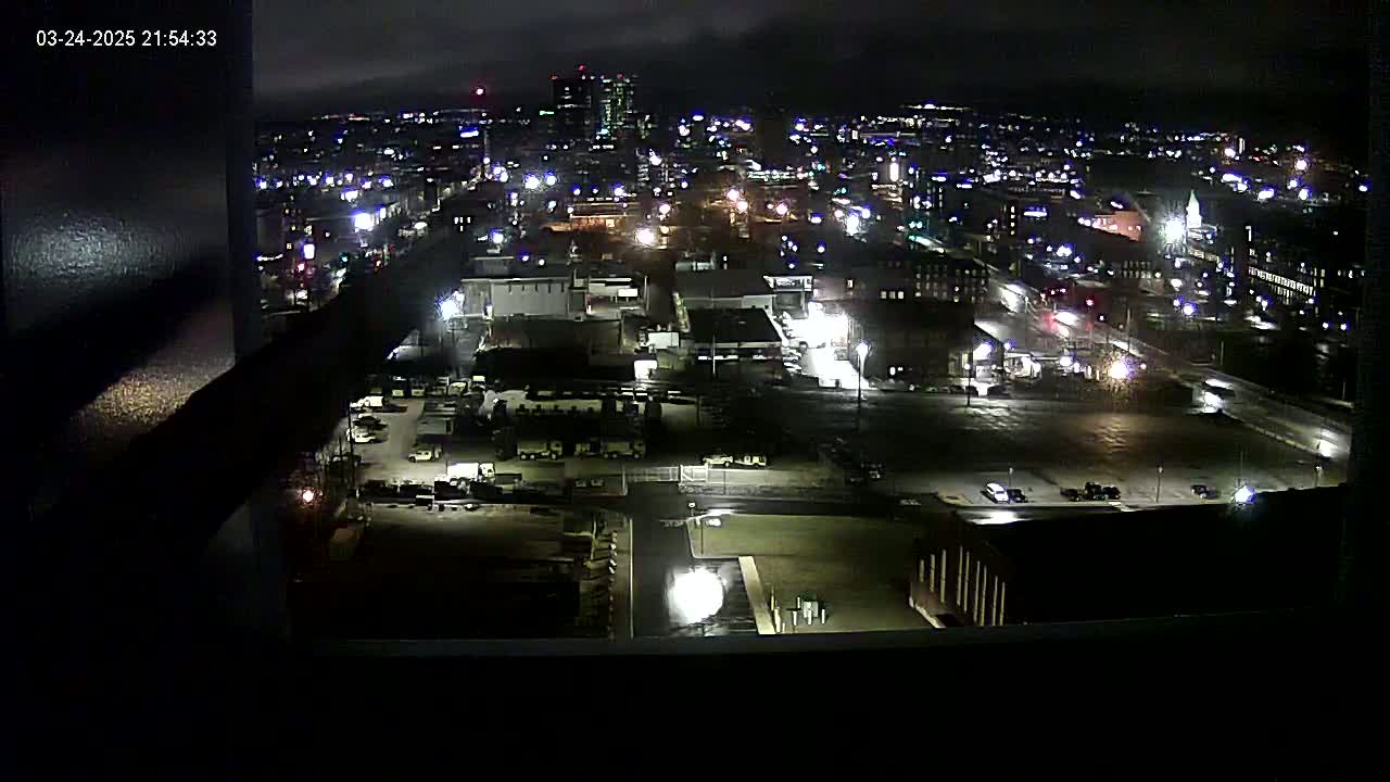 A nighttime, high-angle view of a city's illuminated streets and buildings, with overcast skies.