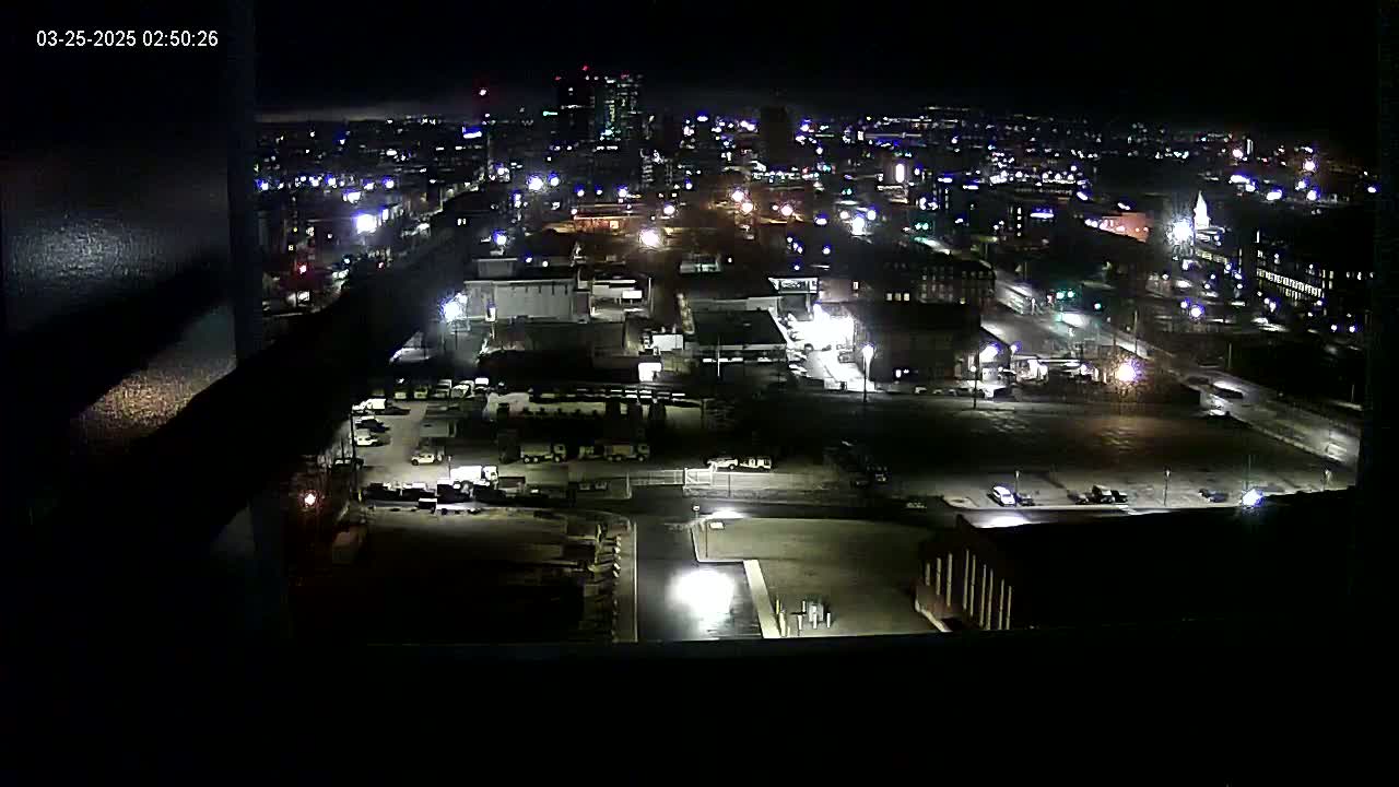 A nighttime, high-angle view of a city's industrial and residential areas, illuminated by streetlights and building lights.