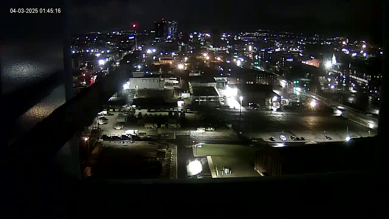 A nighttime, high-angle view of a city's industrial and residential areas, illuminated by streetlights and building lights.