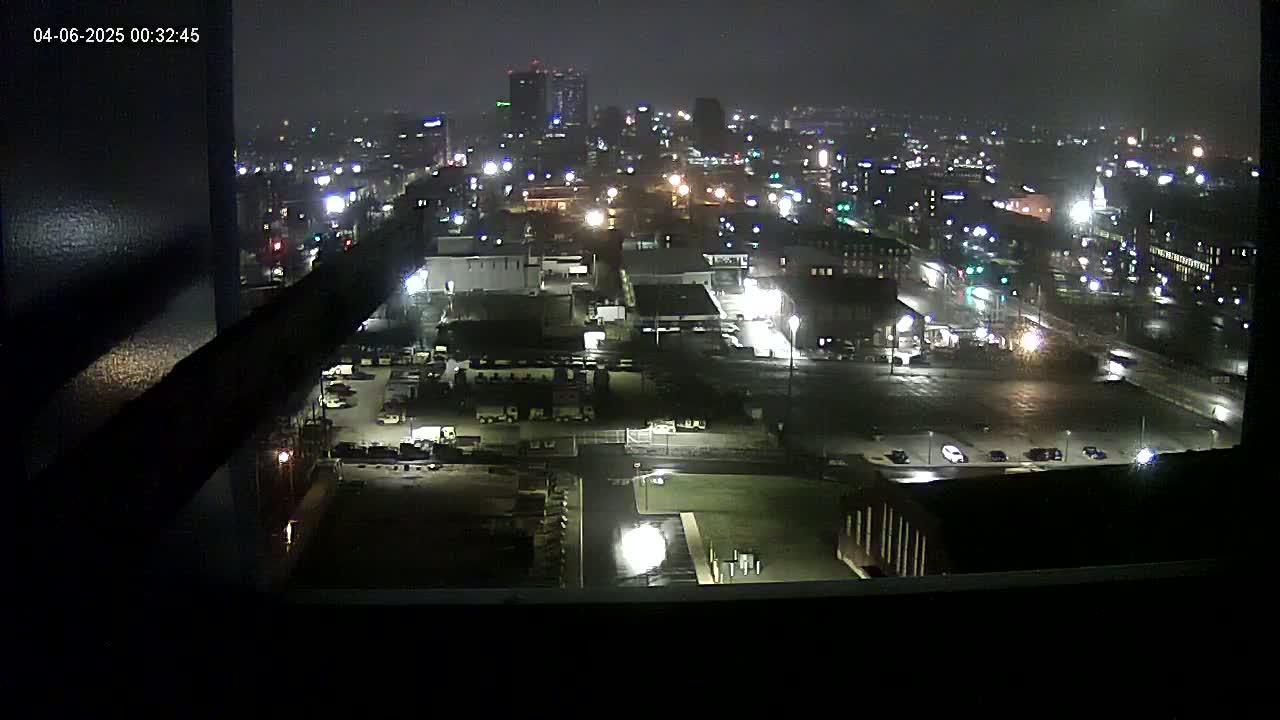 A nighttime view of a city's illuminated cityscape and industrial area, possibly slightly hazy.