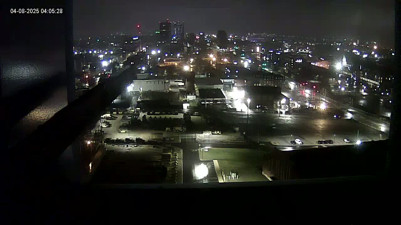A nighttime, high-angle view of a city illuminated by streetlights and building lights under overcast skies.