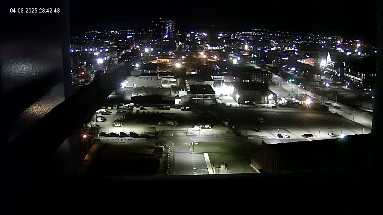 A nighttime, high-angle view of a city's illuminated streets, buildings, and parking lots.