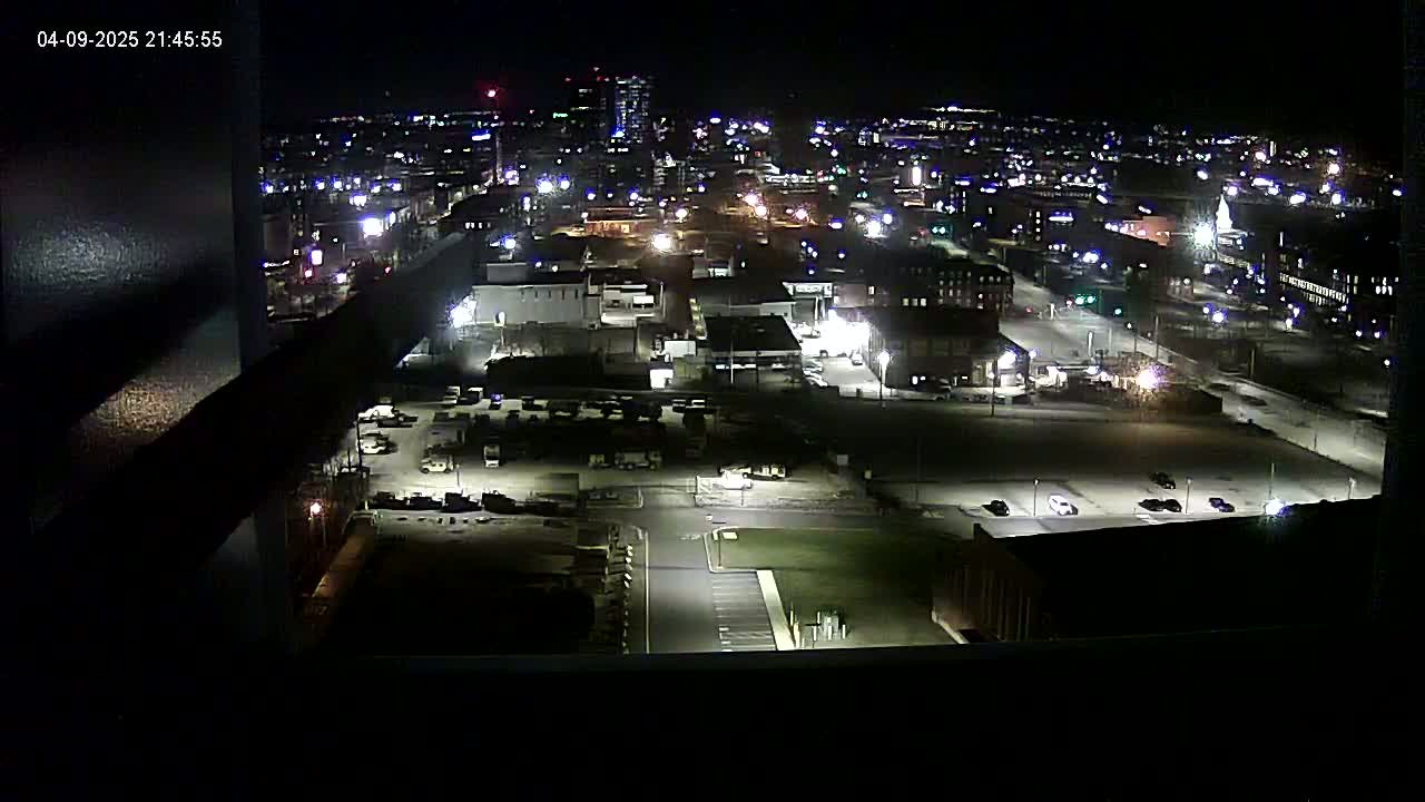 A nighttime, high-angle view of a city's industrial area and surrounding buildings, illuminated by streetlights and building lights.
