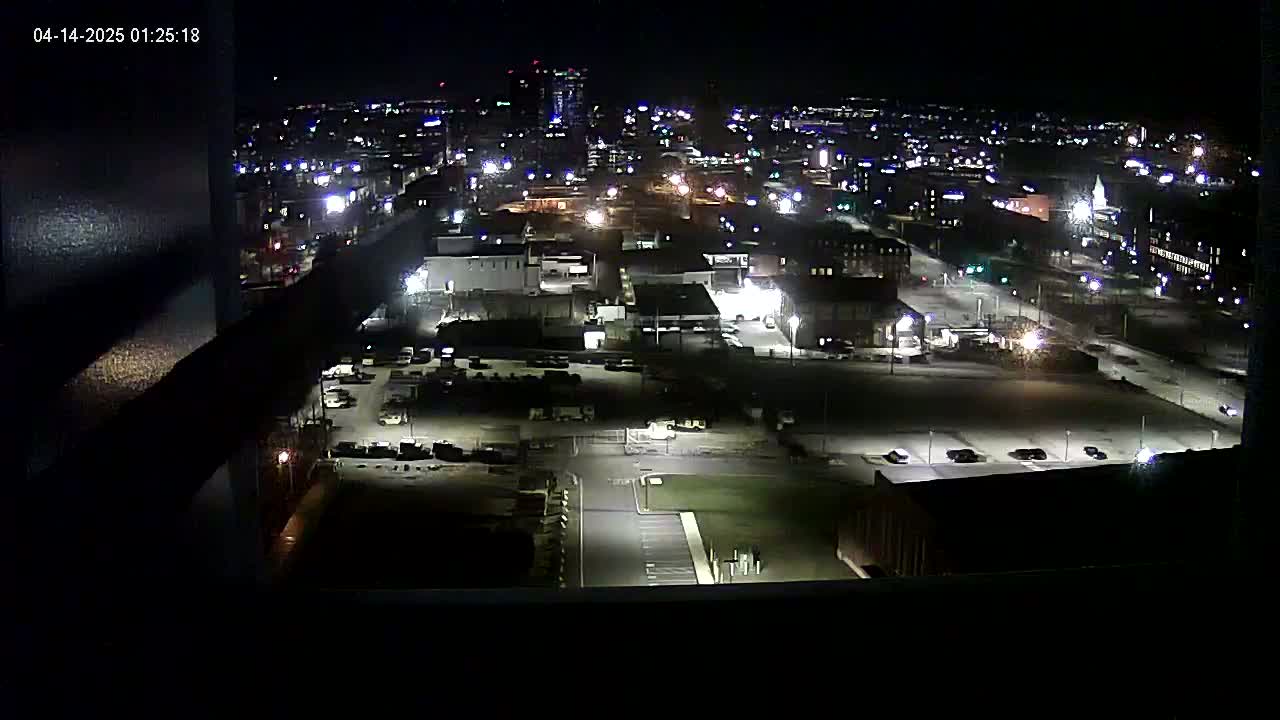 A nighttime view of a city's industrial area and surrounding buildings, illuminated by artificial lights.